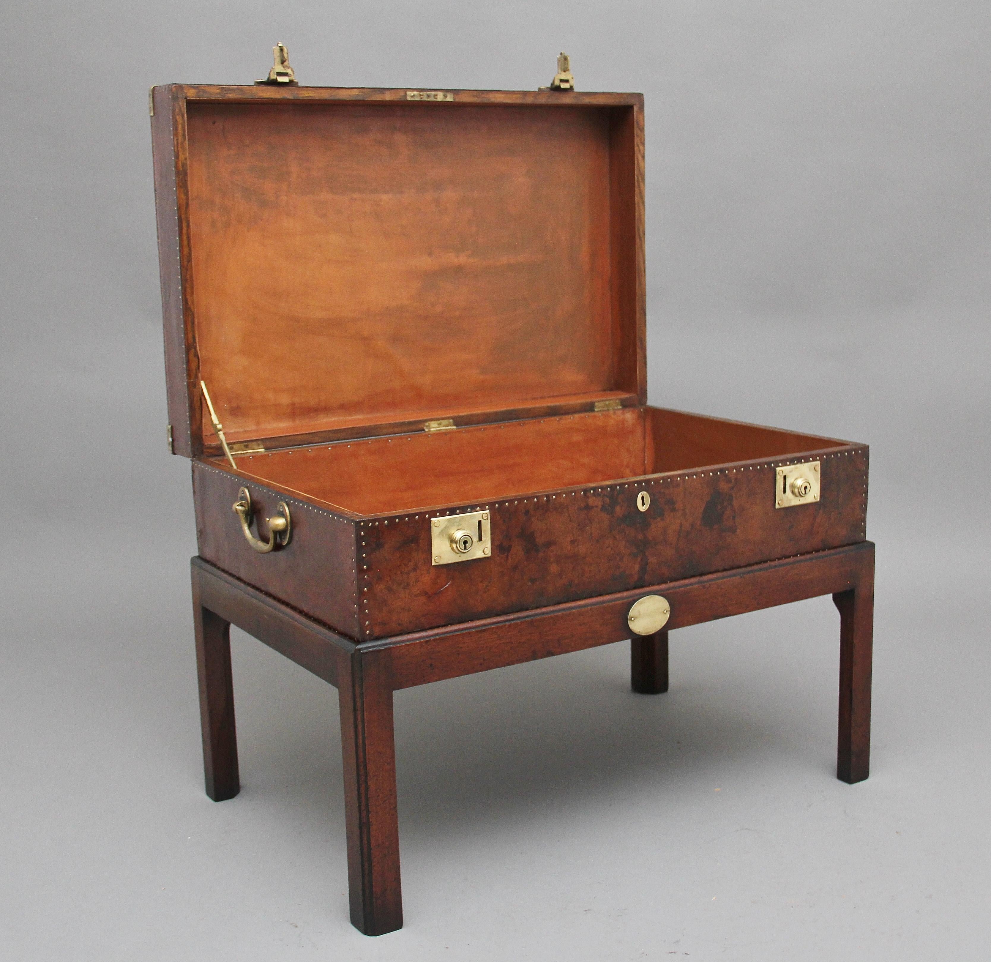Early 20th century leather bound ex army trunk on stand with brass corners, copper studs and brass carrying handles on the sides, on the top of the trunk there is a regimental badge which belongs to the home counties, the hinged top opens to reveal