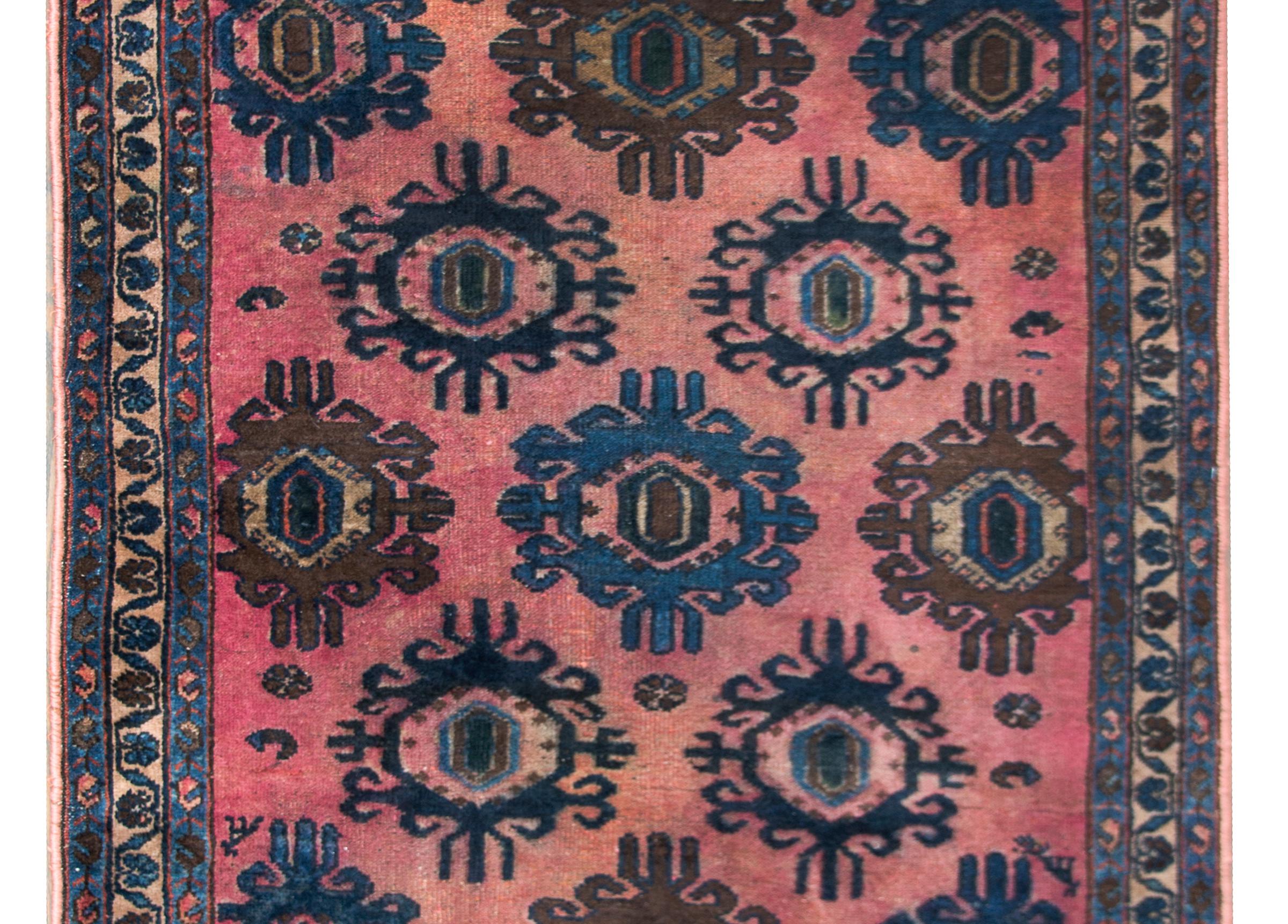 A wonderful early 20th century Persian Lilihan rug with an unusual repeated large-scale stylized floral medallions woven in light and dark indigo, brown, and pink set against an abrash pink background. The border is simple, with three thin stripes