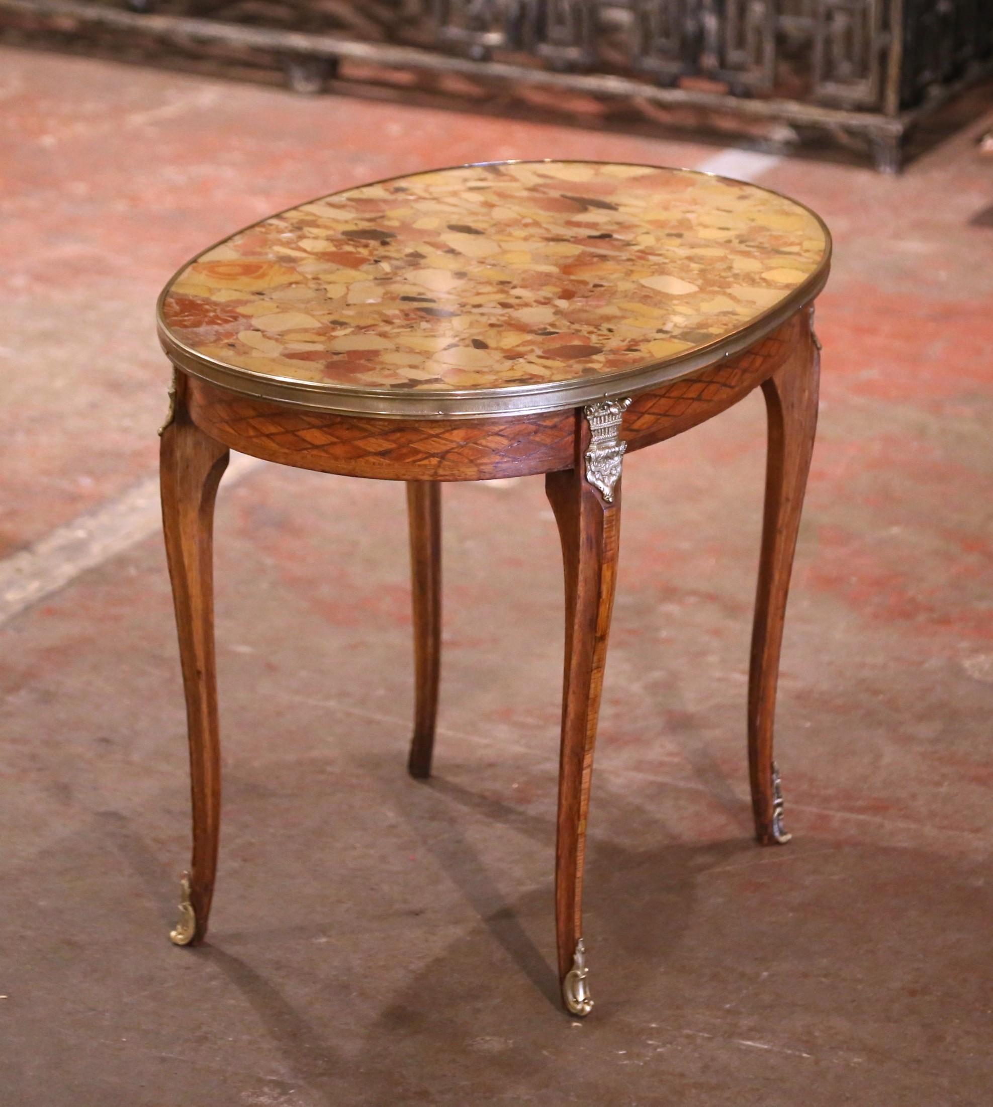 Fabriquée en France vers 1920 et construite en noyer, la table ovale repose sur quatre pieds cabrioles décorés de montures en laiton aux épaules, se terminant par des sabots en bronze. La table d'appoint Louis XV présente une marqueterie détaillée