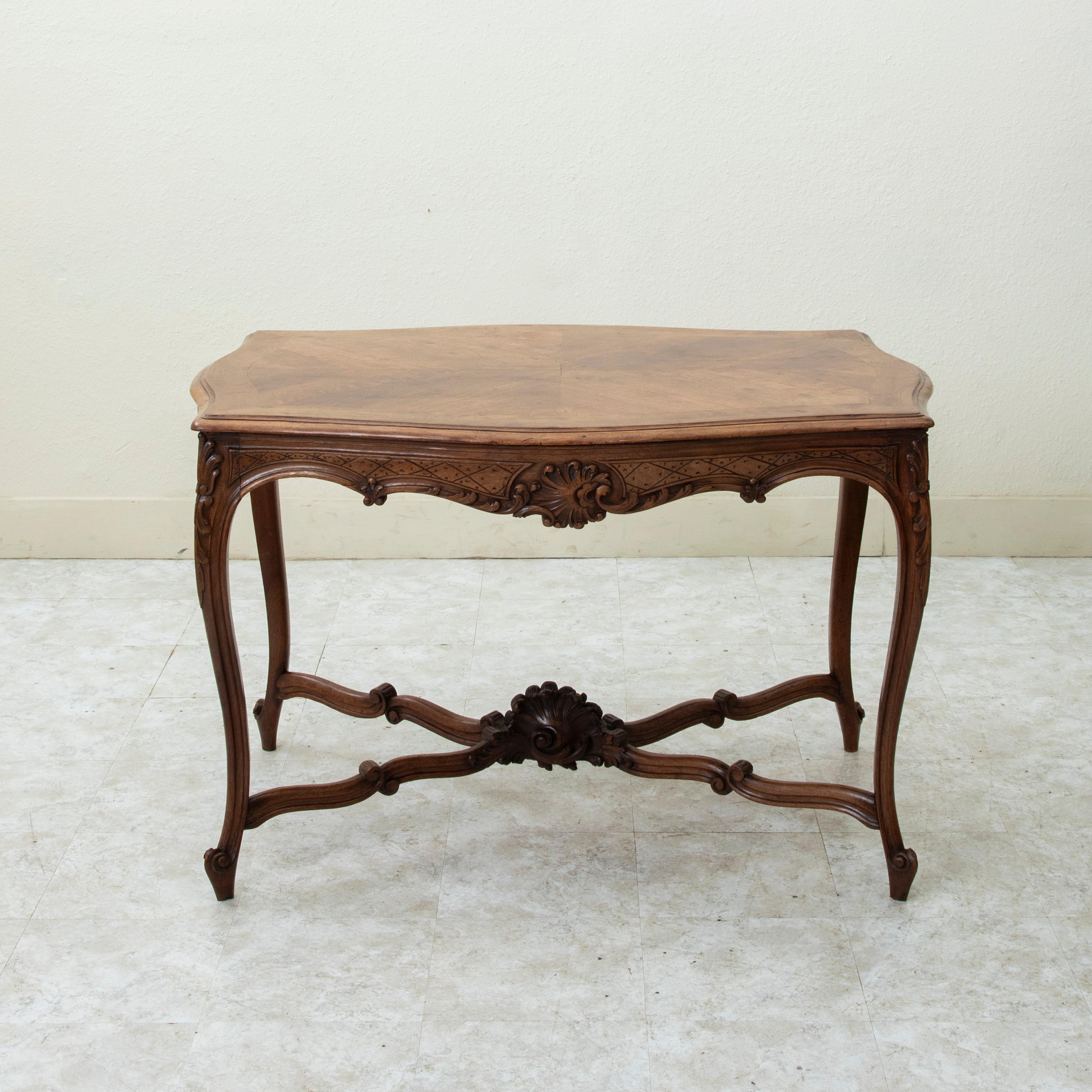 This early twentieth century French Louis XV style walnut writing table features deep relief hand carved details of shells on all four sides and corners as well as scrolling leaves and a diamond pattern motif. The top is a book matched writing
