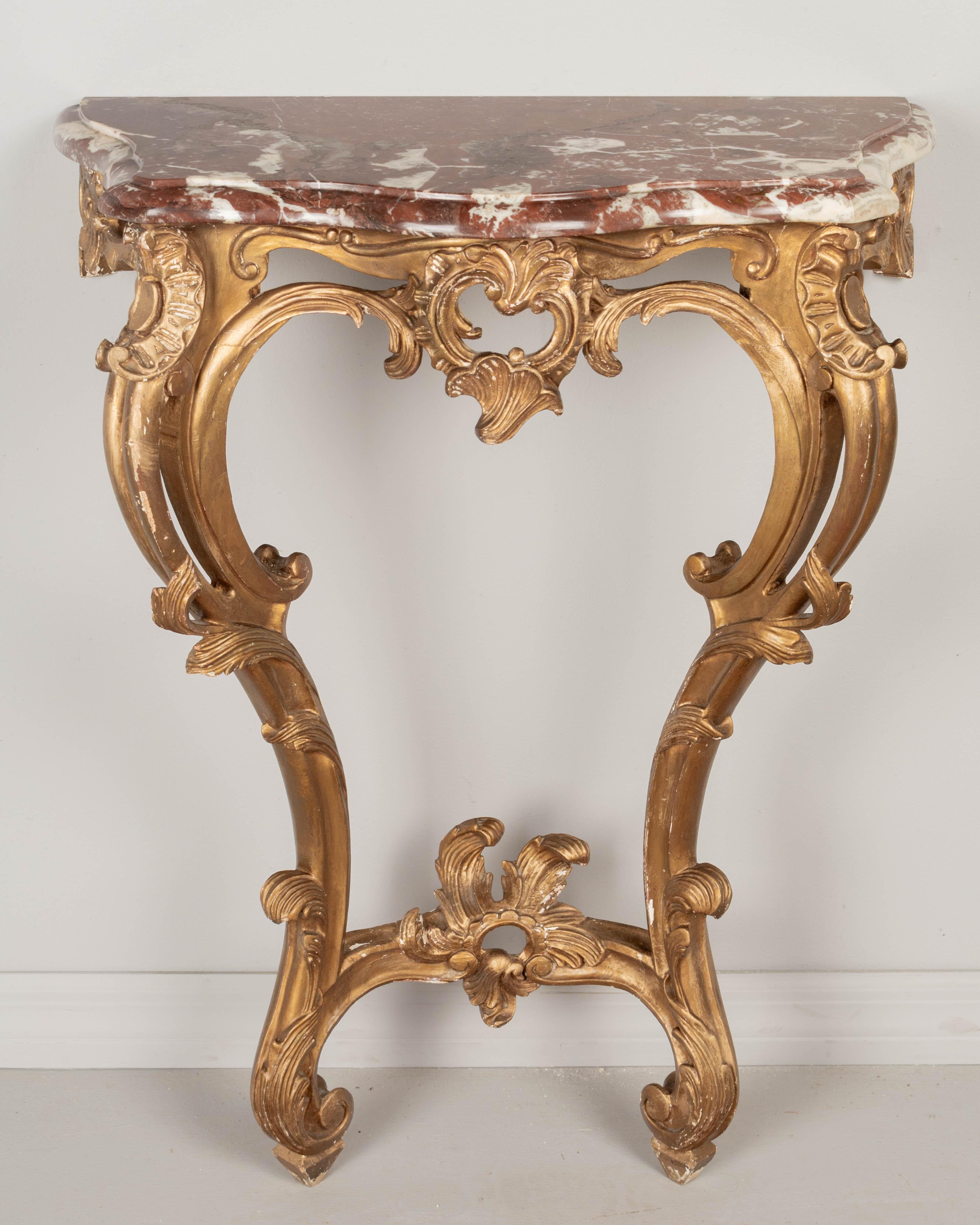 An early 20th century French Louis XV style giltwood console with carved foliate details and warm gold painted patina. Original Rouge Royale marble top. Minor chips and some paint loss. Must be fastened to the wall. Circa 1900-1920.
25.5