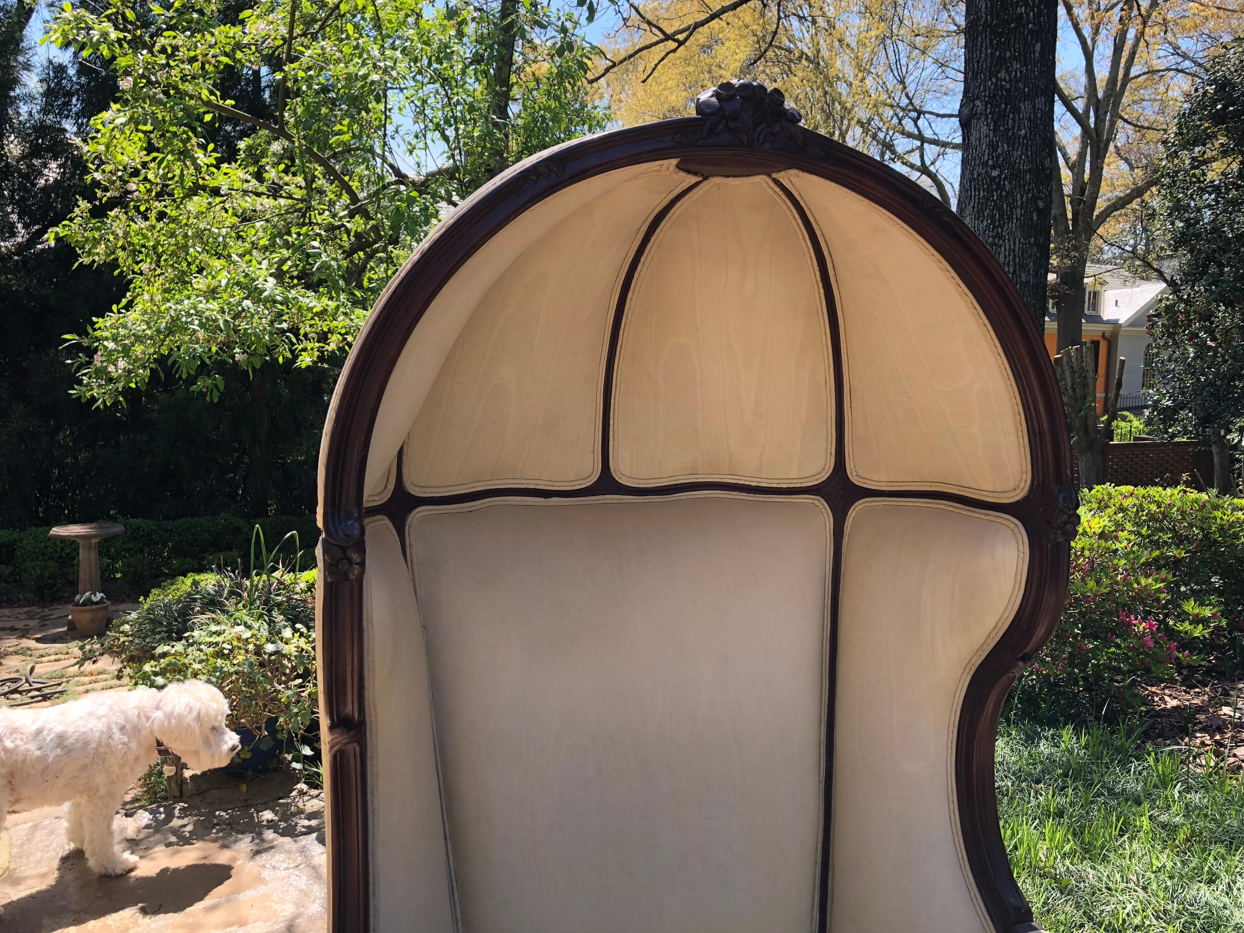 20th Century French Porter’s chair created in the Louis XV style with a walnut frame and carved rosette details.  The canopied chair is currently upholstered in a cream silk taffeta.  