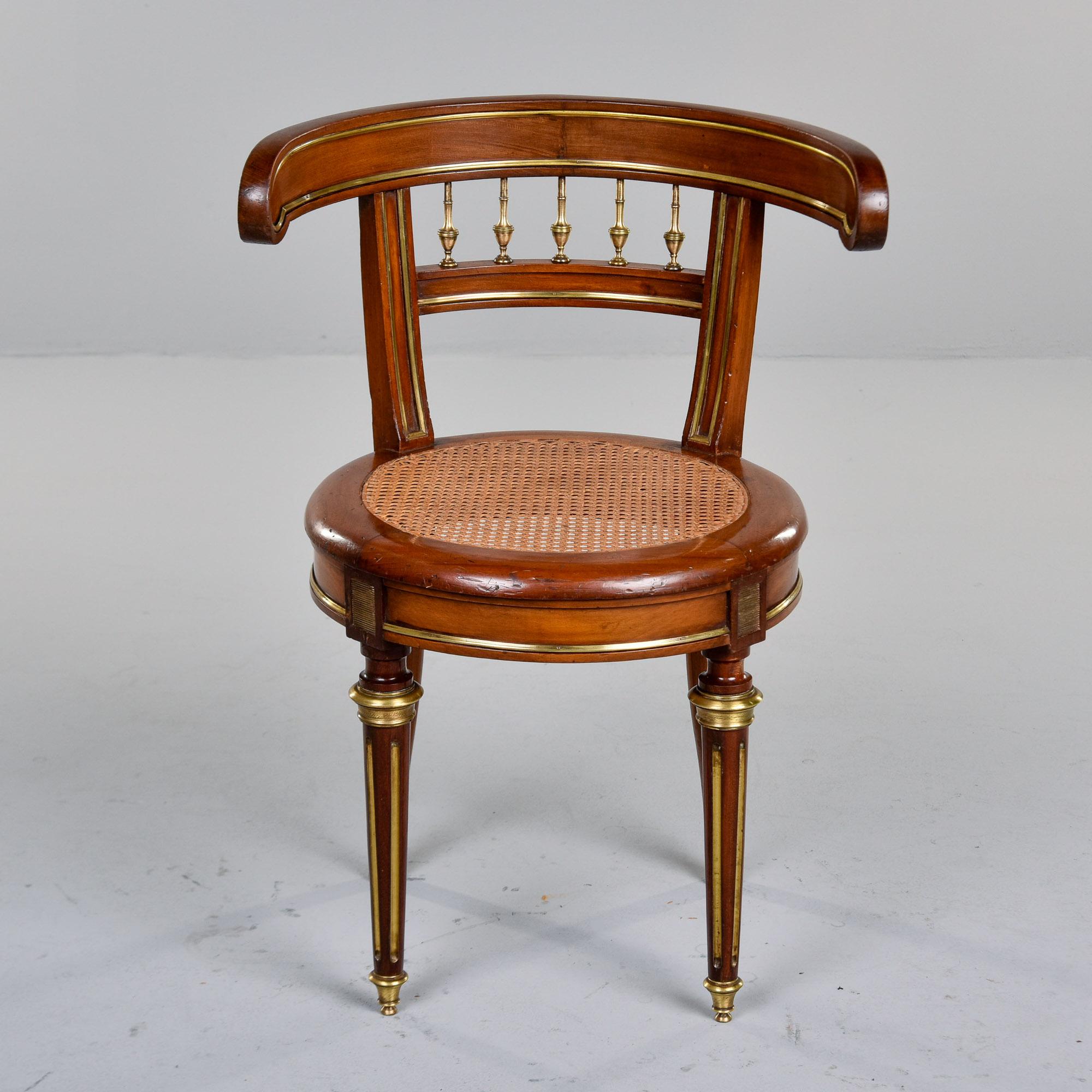 Found in France, this Louis XVI style chair dates from approximately 1910. Frame appears to be mahogany and features a round, caned seat. Legs are reeded, tapered with brass-capped feet and gilt detailing. Decorative brass mounts at base of legs and