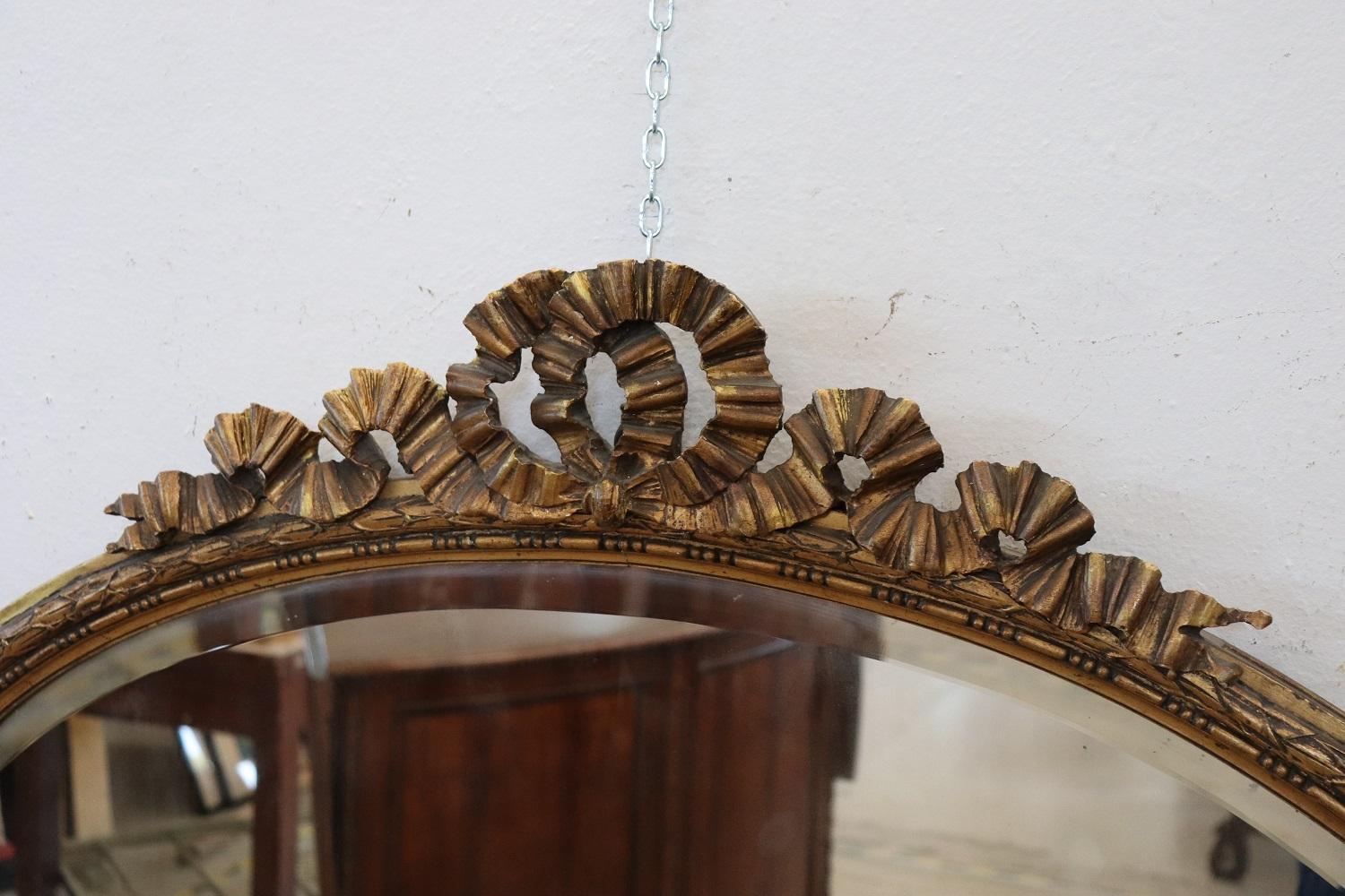 Beautiful elegant oval wall mirror in perfect italian Louis XVI style, 1930s. Hand carved and gilded wood with finely and richly swirls and curls. The gilding has acquired an antique patina.