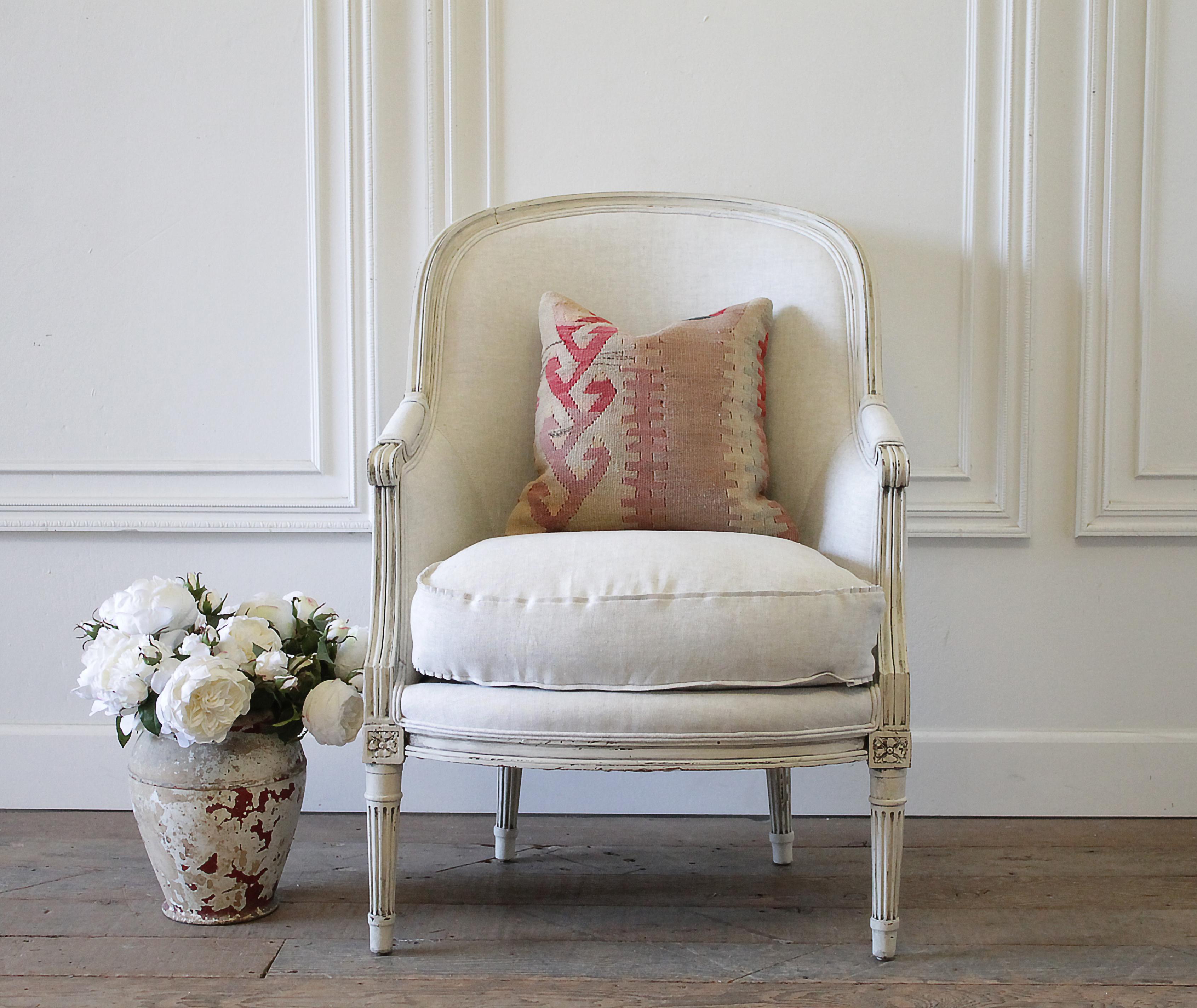 20th century Louis XVI style painted French bergère chair in natural linen frame is painted in our oyster white paint, with natural aged patina and distressed edges. Louis XVI style with fluted legs, and rounded curved back. We reupholstered this