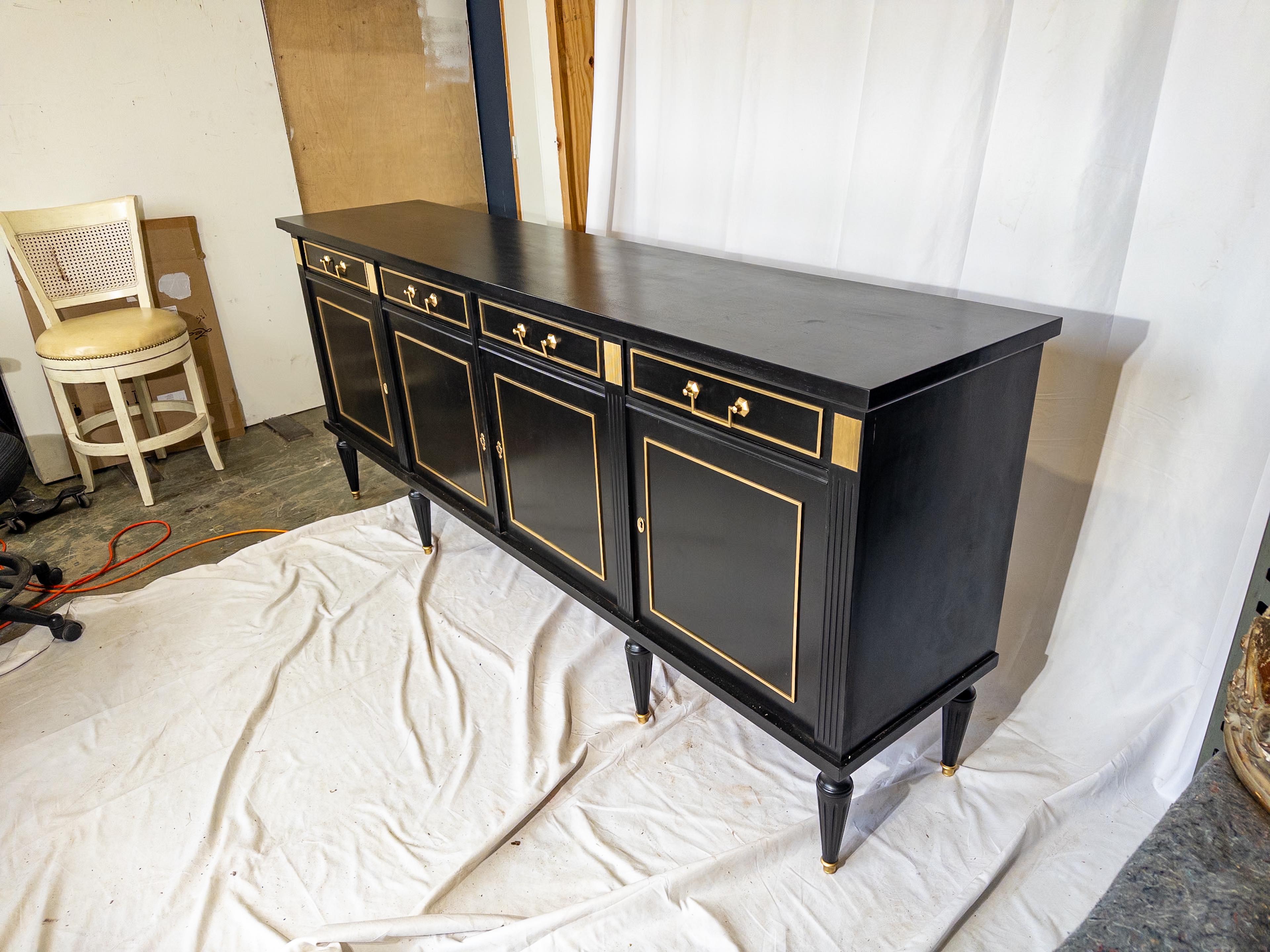 Step into the timeless elegance of the early 20th century with the Louis XVI Style Sideboard, a striking piece that exudes sophistication and grandeur. Painted in a sleek black finish, its surface gleams with an air of refined luxury, enhanced by