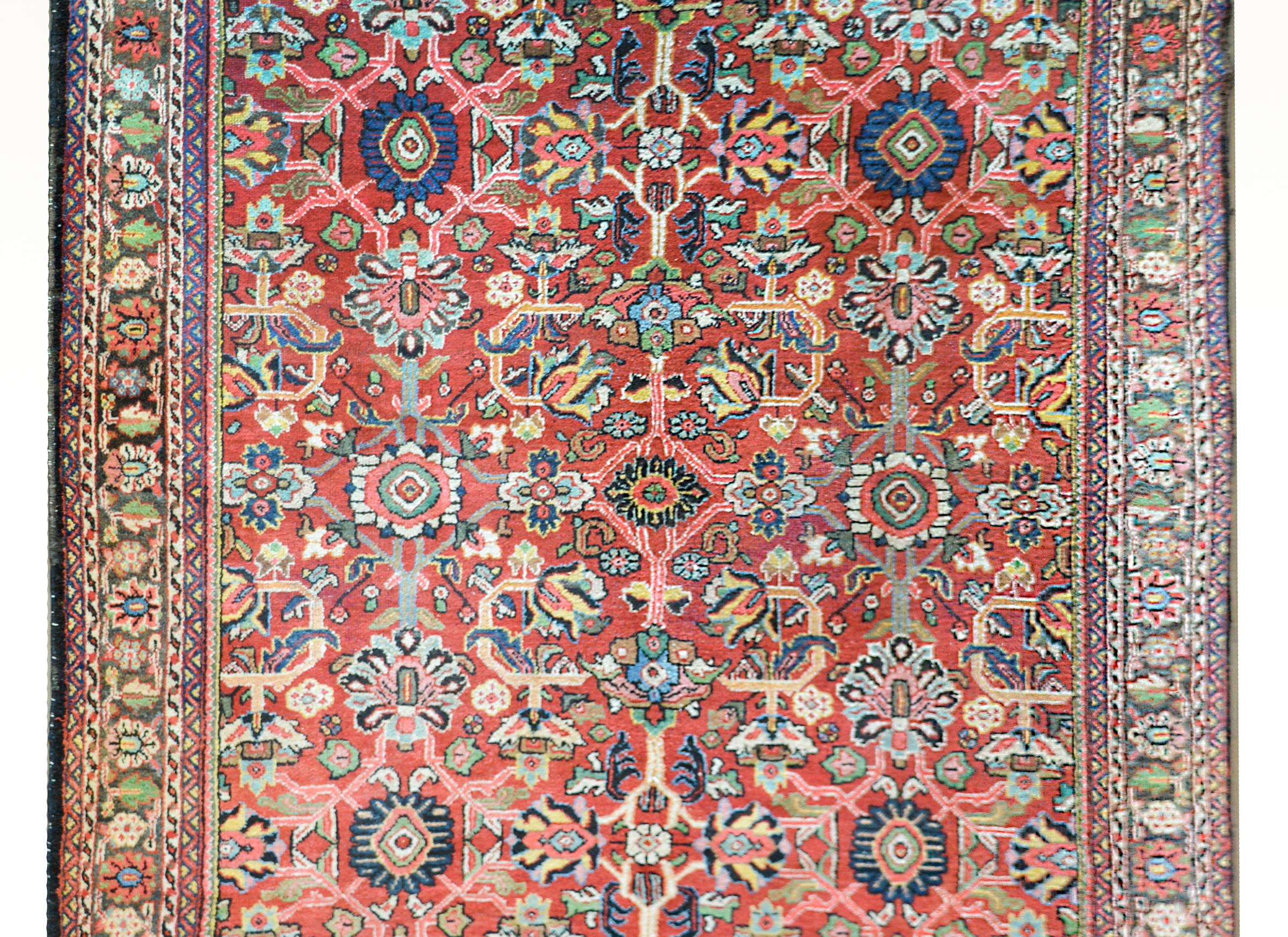 A gorgeous early 20th century Persian Mahal rug with an all-over tribally woven pattern with multiple stylized flowers and scrolling vines woven in myriad colors against a crimson background, and surrounded by a border with multiple stylized floral