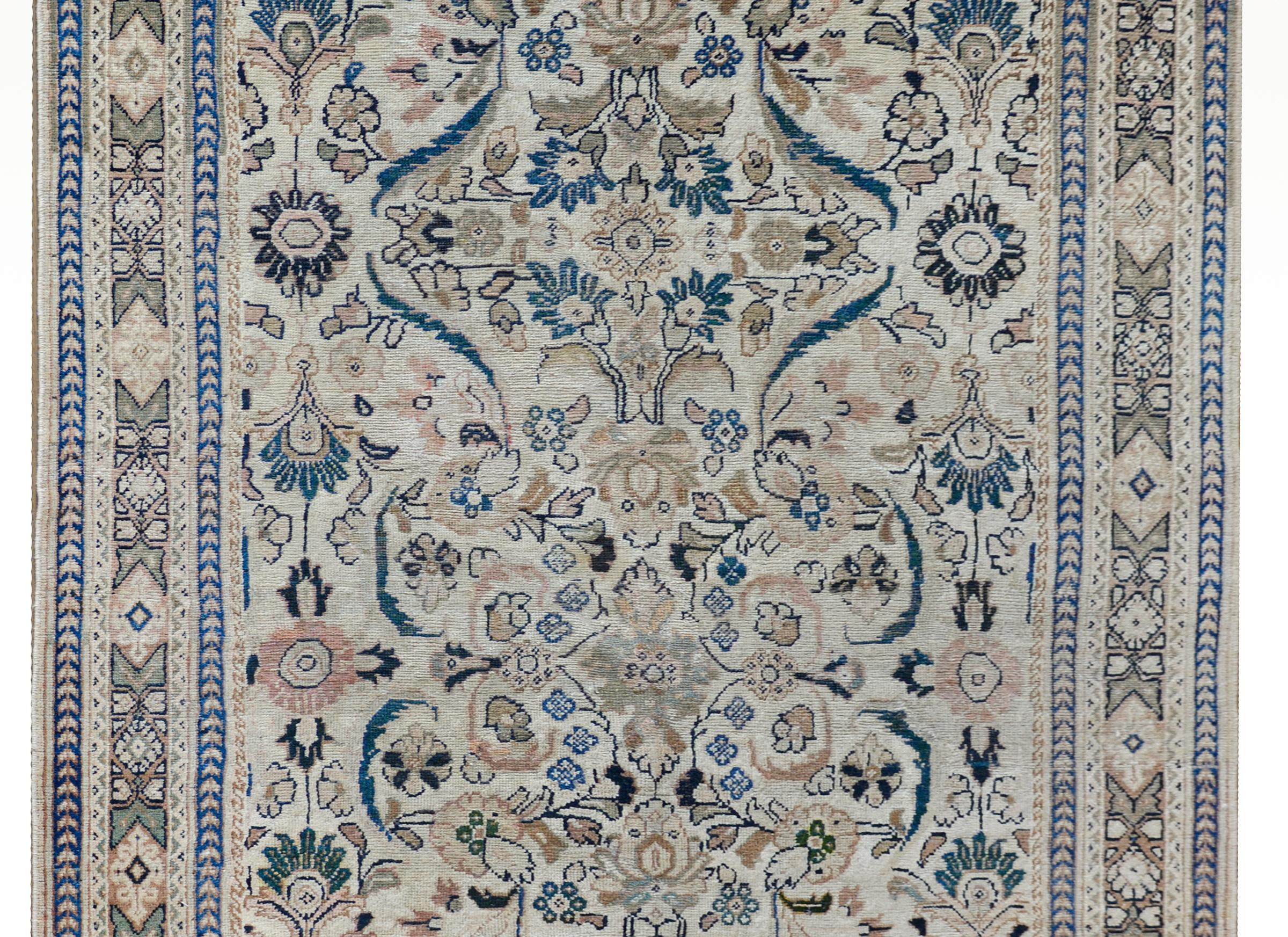A gorgeous early 20th century Persian Mahal rug with a large-scale mirrored floral and scrolling vine patterned field woven in light and dark indigo, pink, green, and cream, and surrounded by a wide border with a central stylized floral patterned