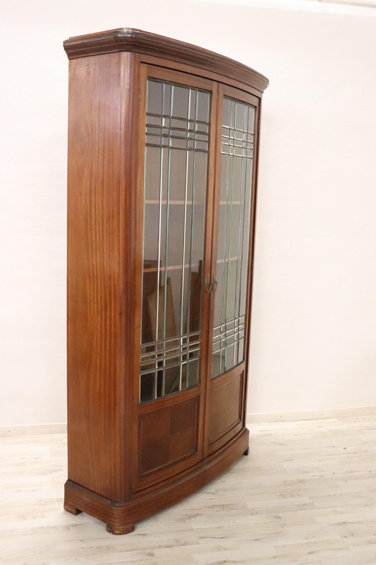 Refined bookcase or showcase early 20th century in mahogany wood. Precious original glass. Very linear and essential perfect to be combined even in a modern home. The upper part with glass doors is perfect for displaying your collection of precious
