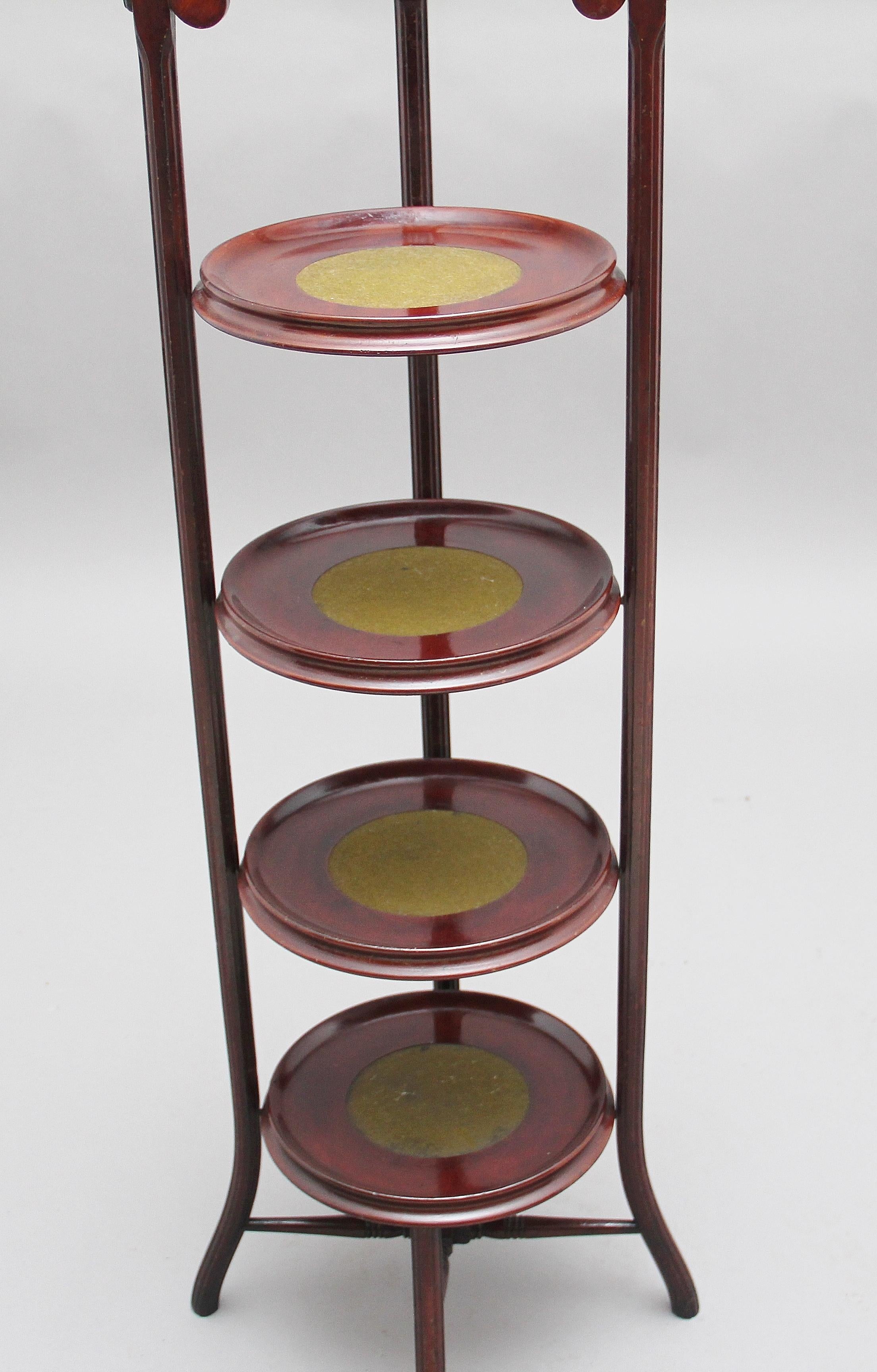 A decorative early 20th century mahogany four-tier cake stand, the four dish shaped tiers having green baize inserts, these are supported on a turned and fluted frame with outswept legs, the top of the cake stand is decorated with a turned finial,