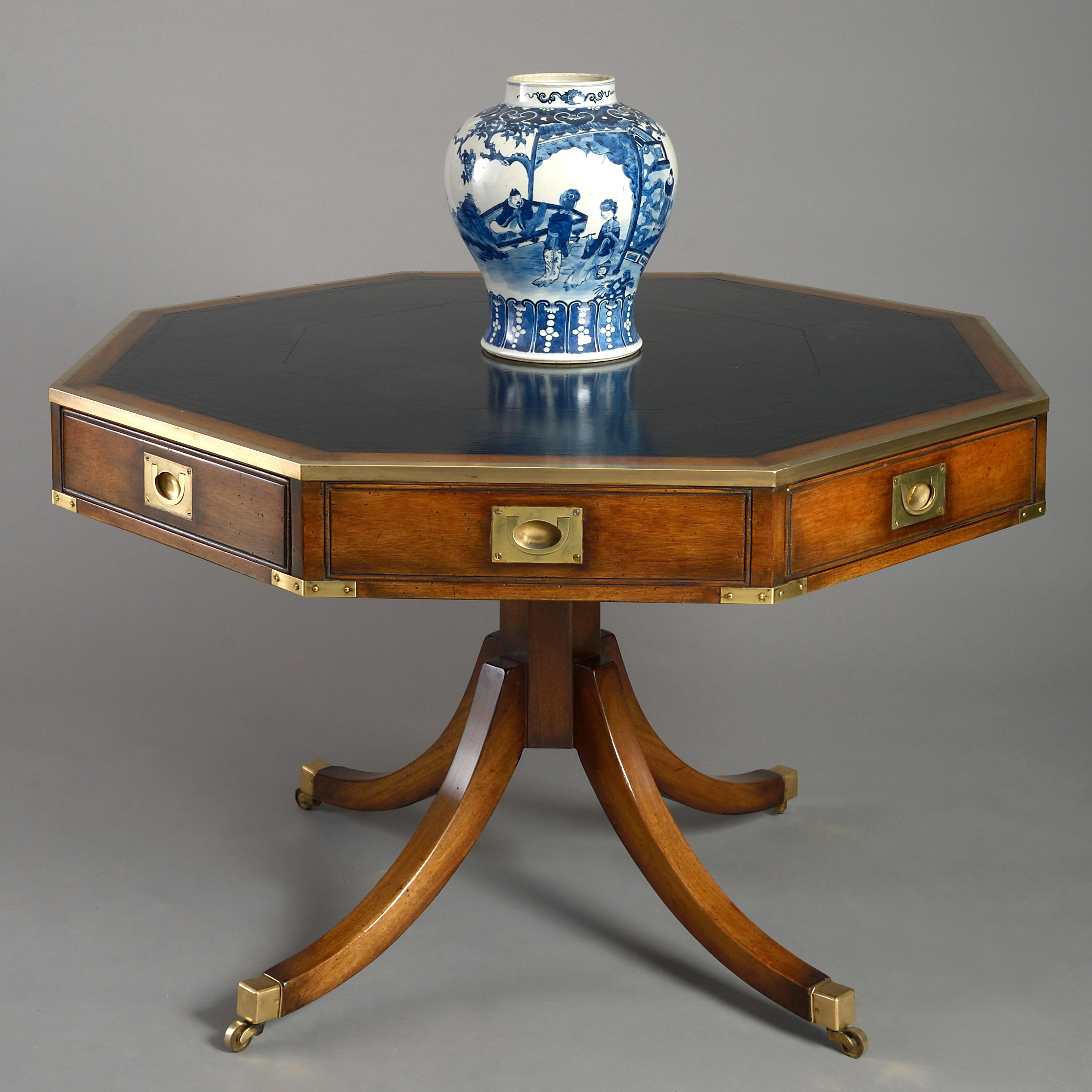 An early 20th century Campaign rent table in the George III manner, the tooled black leather top inset upon an octagonal mahogany drum, having four drawers and four dummy drawers, each with sunken brass handles, raised upon a faceted stem and