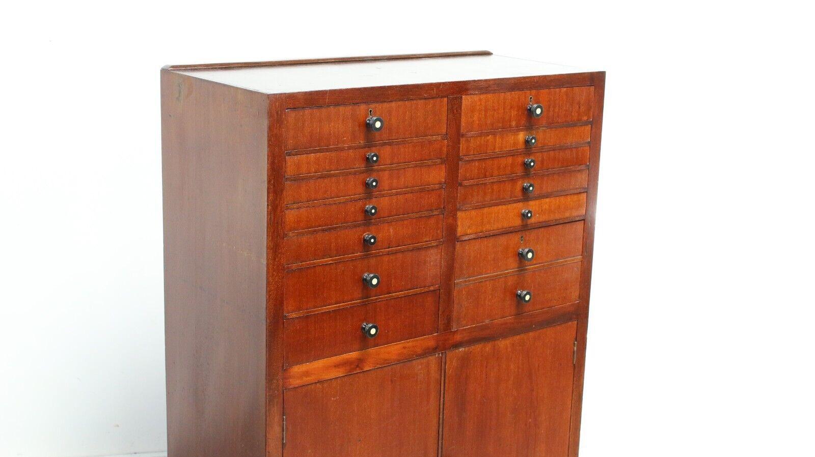 This early 20th century Mahogany dentist cabinet has eight small drawers, four medium size drawers and a cabinet with doors under, all with original ebonised handles. 

This cabinet adds a certain level of charm to the piece and makes it an