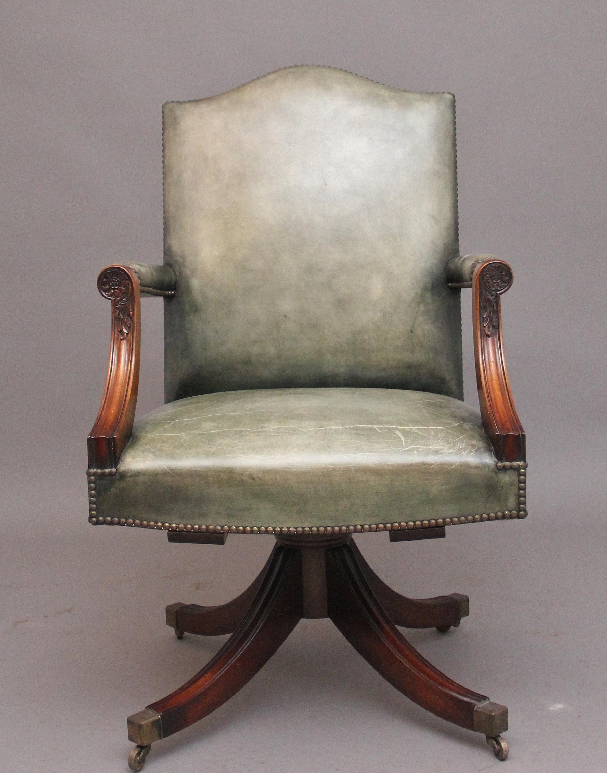 Charmante chaise de bureau pivotante en acajou du début du 20e siècle, avec un dossier haut en forme et une assise rembourrée tapissée de cuir vert clair et décorée de clous en laiton, des supports d'accoudoirs en acajou avec un décor sculpté,