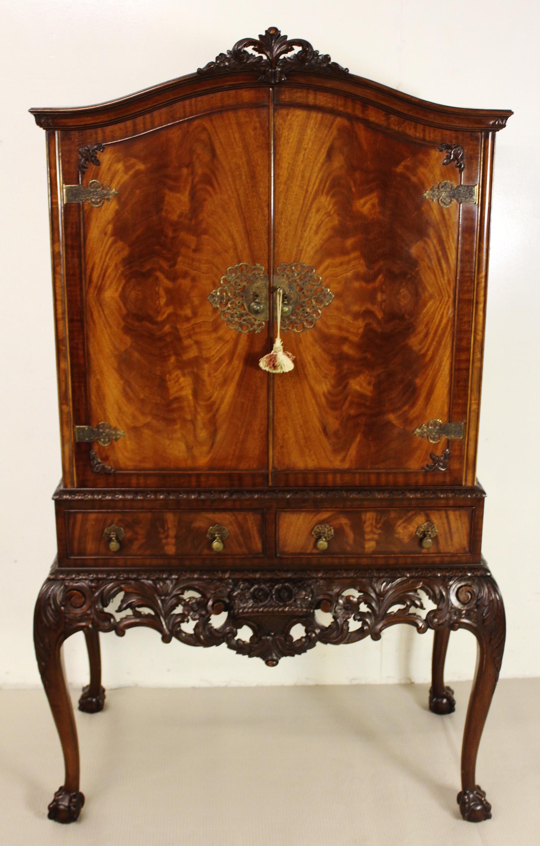 A stunning cocktail, or drinks, cabinet in flame mahogany. The domed top cabinet stands on an elaborately carved mahogany Stand. The cabinet is fitted with attractive flame mahogany veneers and is surmounted by a carved crest. There are elaborate