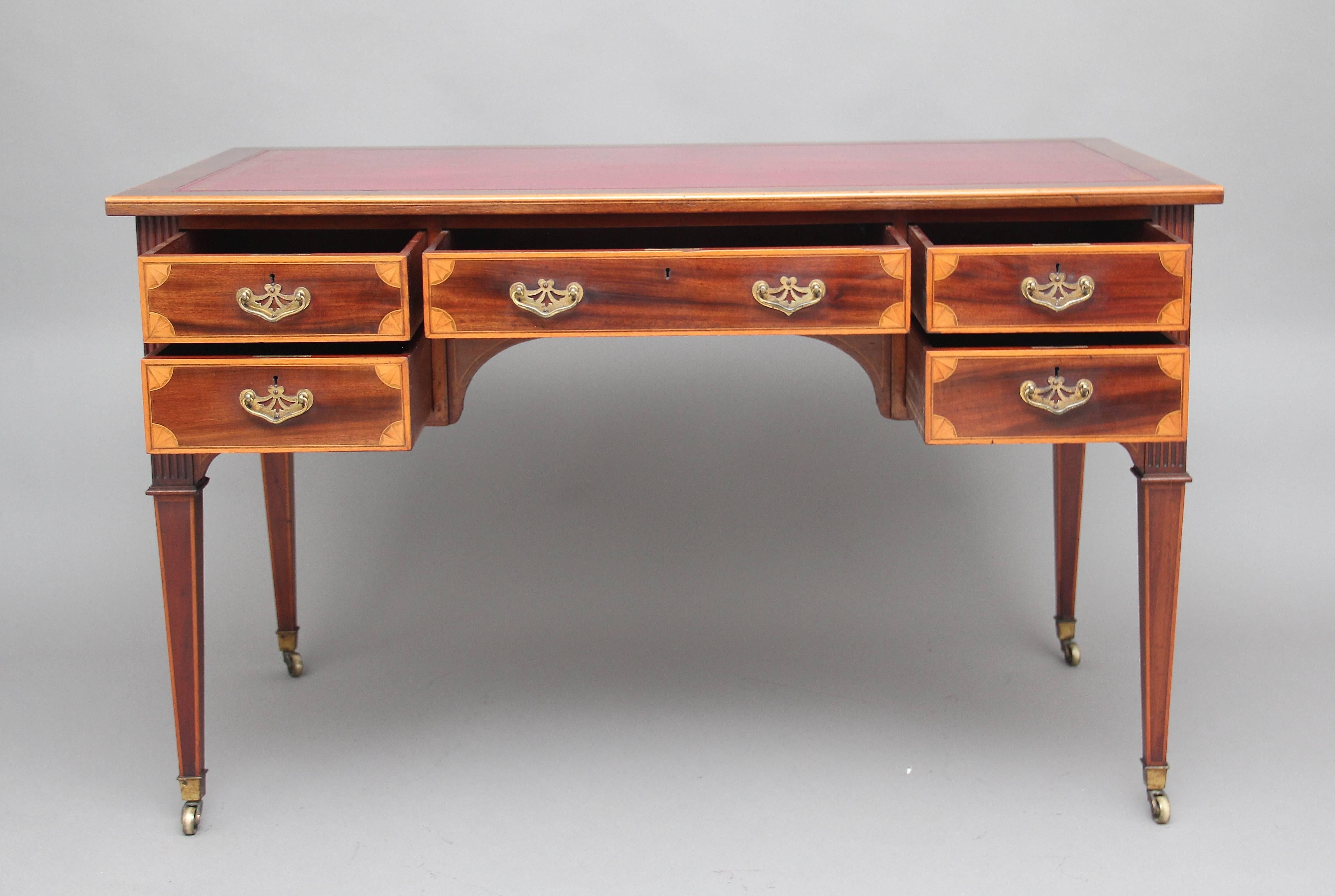 Early 20th century mahogany inlaid writing table, the top having a red leather writing surface decorated with gold tooling, with a combination of five mahogany lined drawers, original brass handles, the drawers fronts having boxwood inlay and inlaid