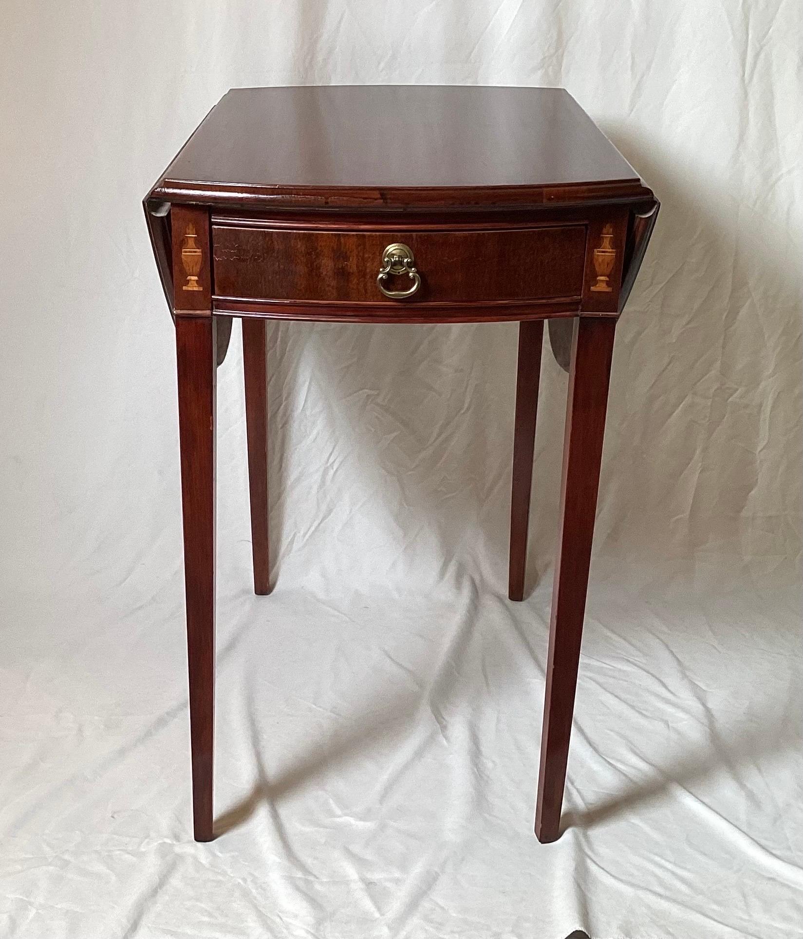 A classic diminutive mahogany and satinwood Pembroke dropleaf table.  The table with center drawer with a D shaped leaf on each side with delicate urn satinwood inlay on the top of the tapering legs.  Table with leaves down measures 26 deep, 18