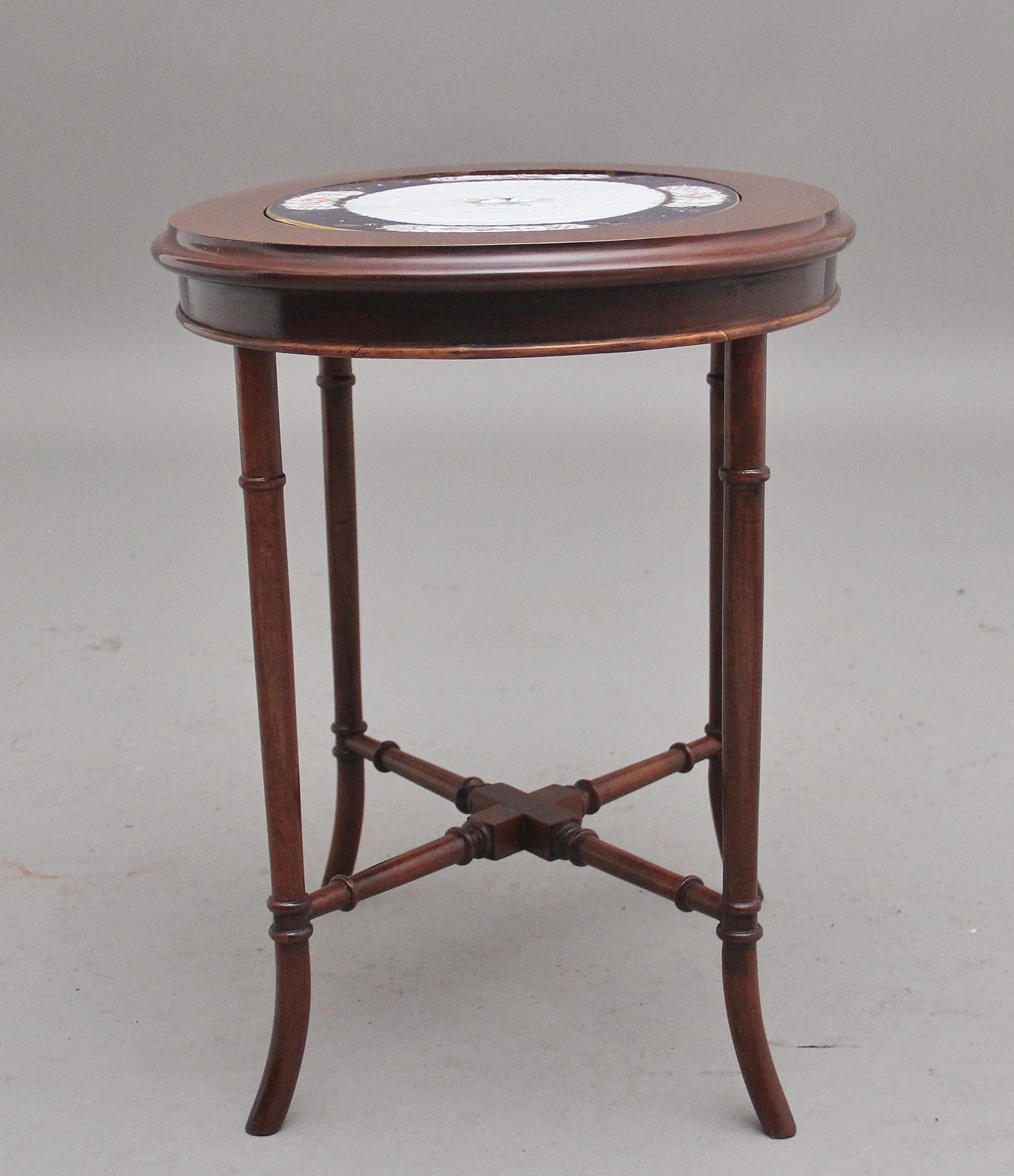 Early 20th century mahogany occasional table with a ceramic inset, having an oval moulded edge top with a decorative oval ceramic plate incorporating floral decoration and a navy blue border, supported on turned outswept legs united by a cross