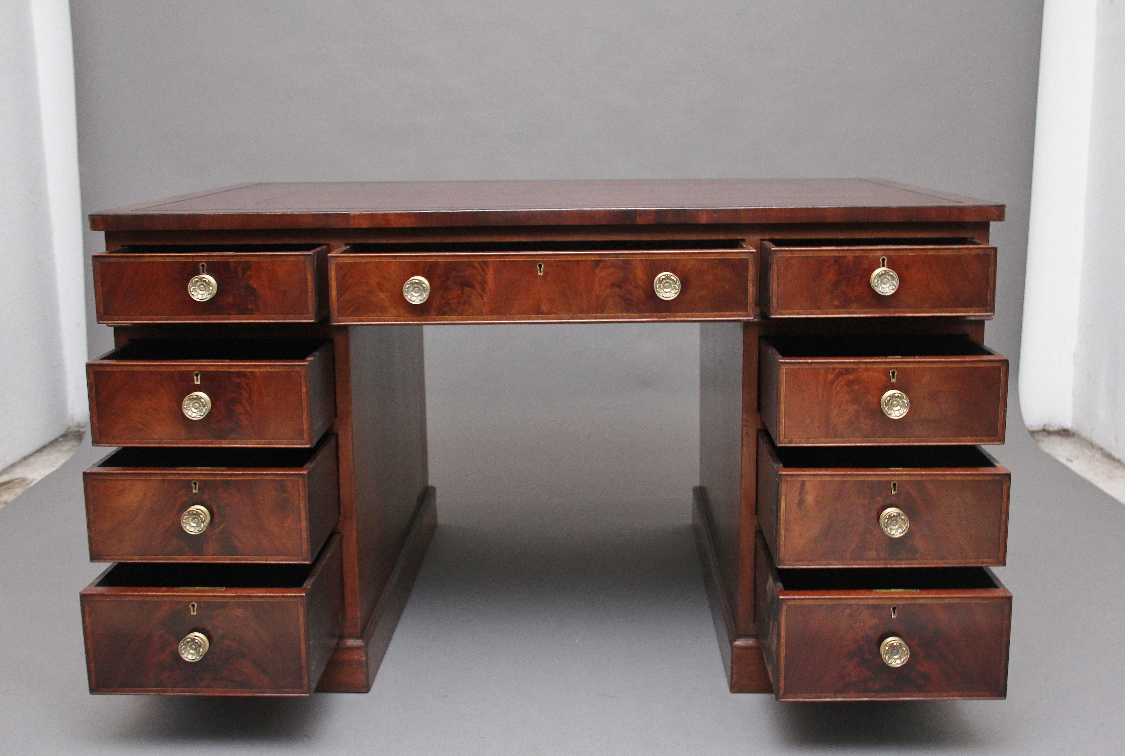 Early 20th century mahogany twin pedestal partners desk, the top having a tan brown leather writing surface decorated with gold and blind tooling, the front of the desk having an arrangement of nine graduated, oak lined drawers with engraved brass