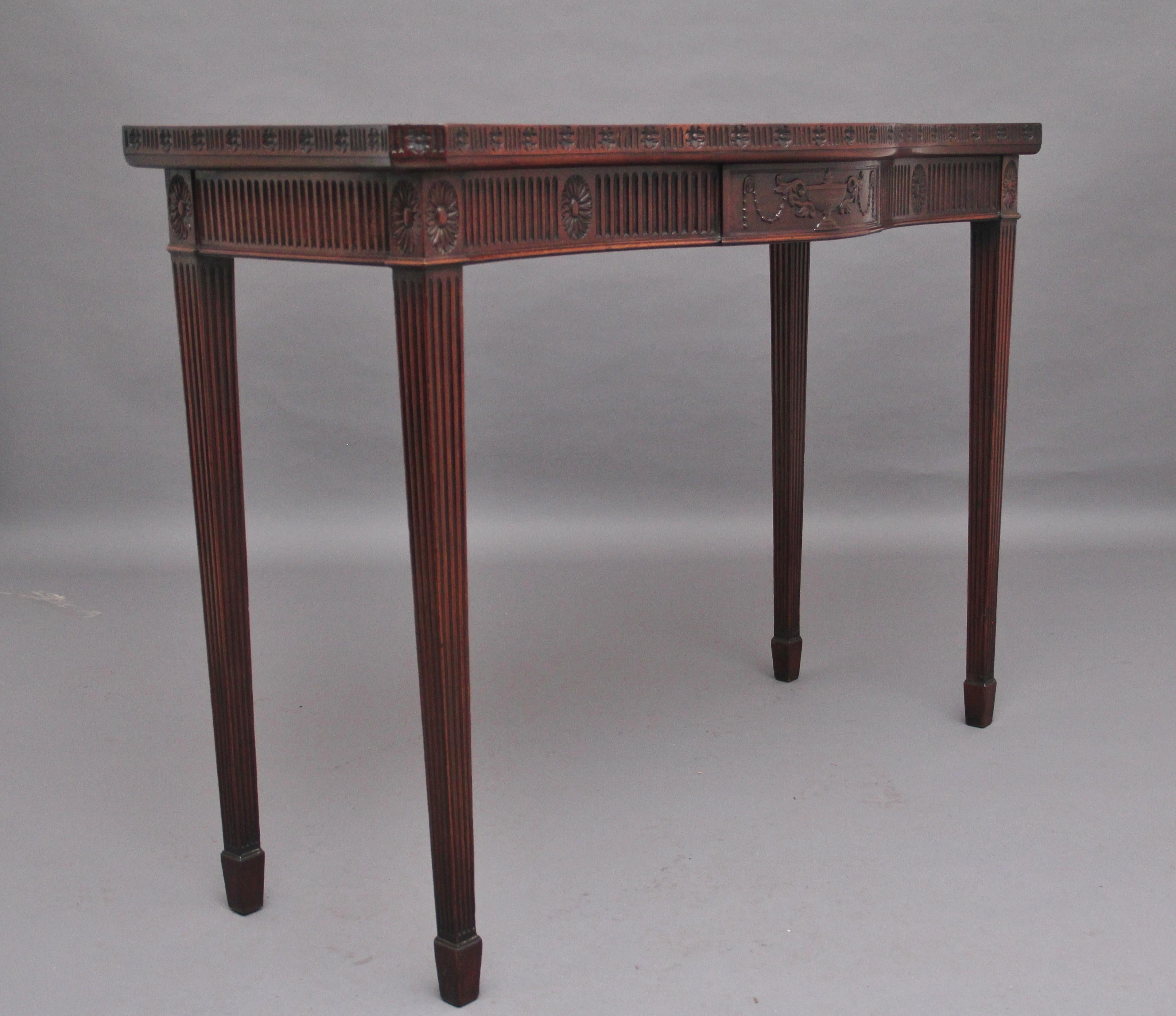Early 20th Century mahogany serpentine console table in the Adam style, the wonderfully figured top above a fluted frieze, the frieze decorated with floral carving and a central plaque with a carved urn, the sides of the serving table has the same