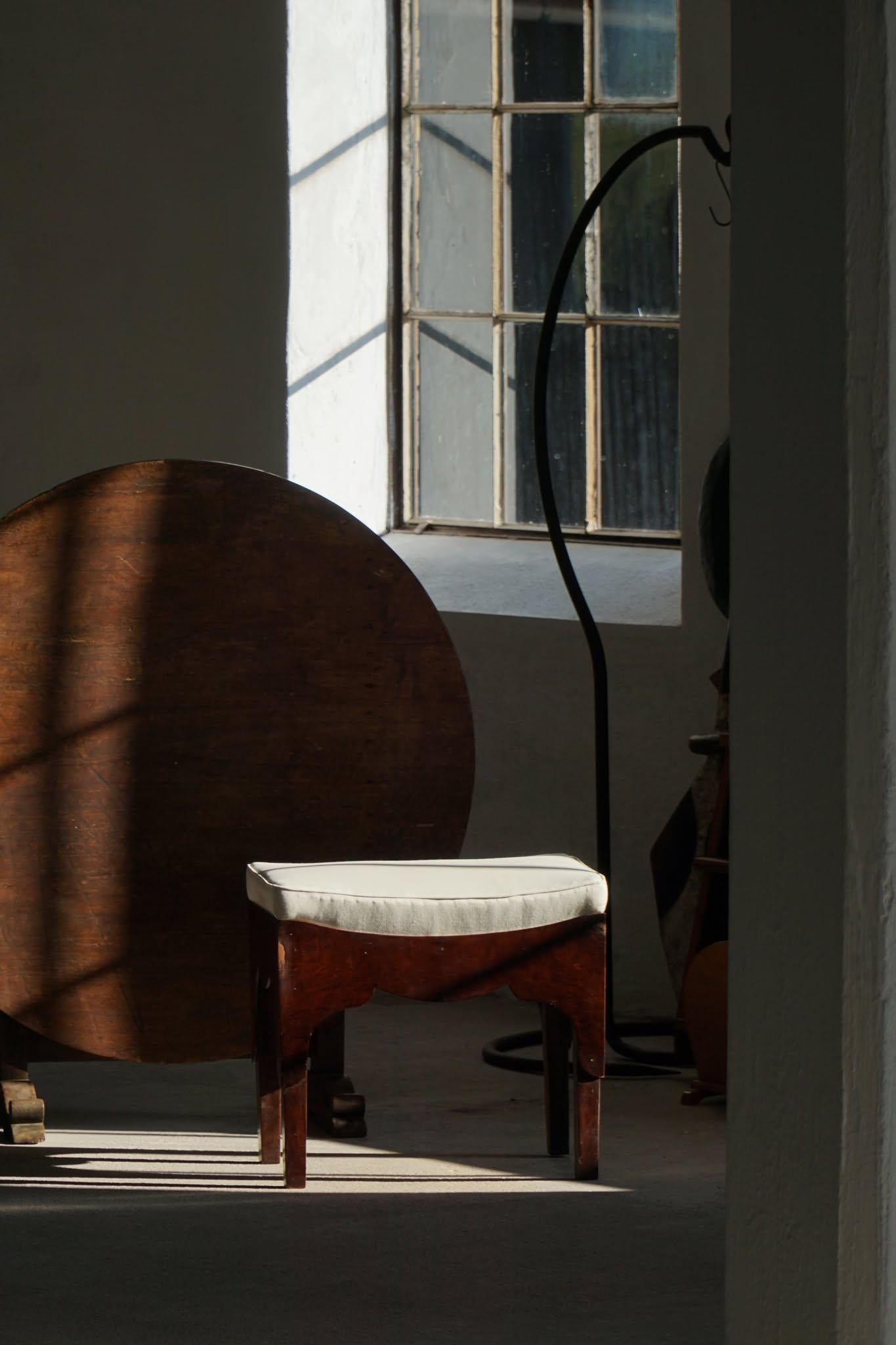 A charming early 20th century dressing or vanity stool, crafted from richly toned mahogany. Made by a Danish Cabinetmaker. 

The seat is upholstered in a neutral light fabric, likely a later re-covering, providing a versatile look that complements