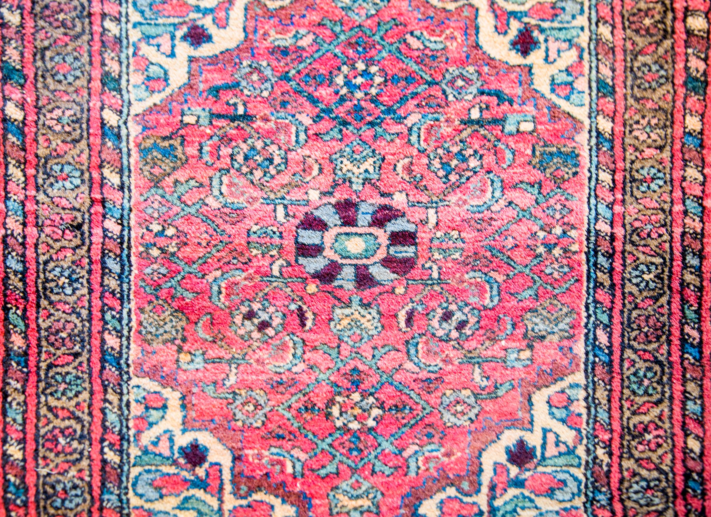 A gorgeous early 20th century Persian Malayer rug with a beautiful central flower medallion amidst an all-over field of flowers on a cranberry background. The border is traditional, with a central petite floral and vine stripe flanked by matching