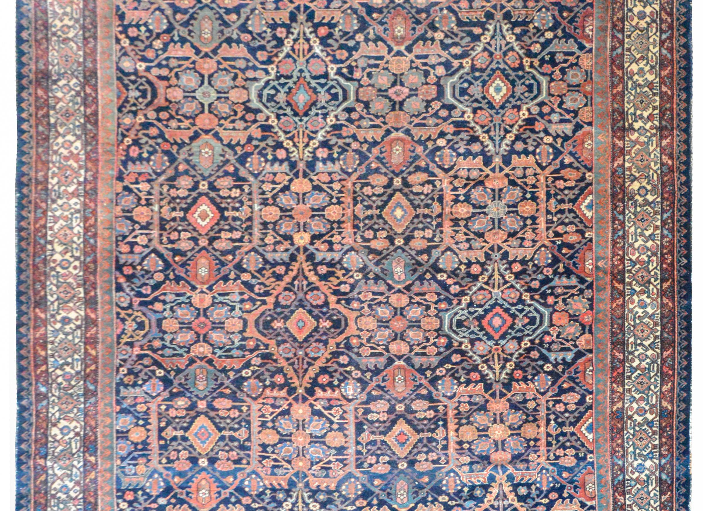 A wonderful early 20th century Persian Malayer rug with a repeated mirrored floral trellis pattern woven crimson, pink, light indigo, and cream, set against a dark indigo background, and surrounded by a border containing multiple petite floral