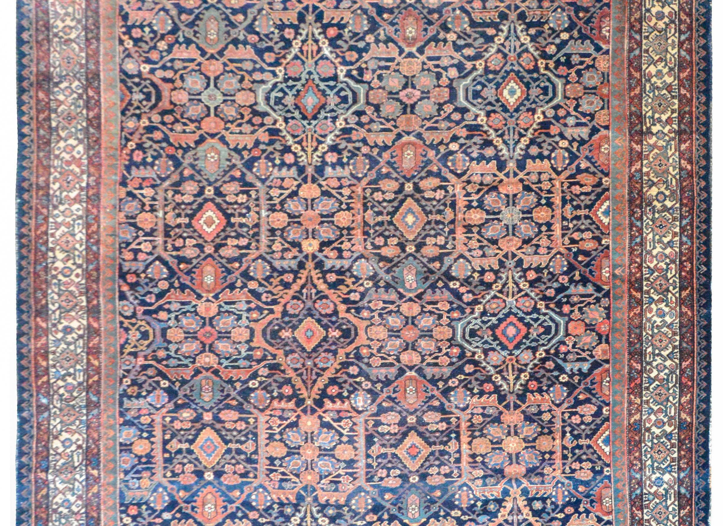 A wonderful early 20th century Persian Malayer rug with a repeated mirrored floral trellis pattern woven crimson, pink, light indigo, and cream, set against a dark indigo background, and surrounded by a border containing multiple petite floral