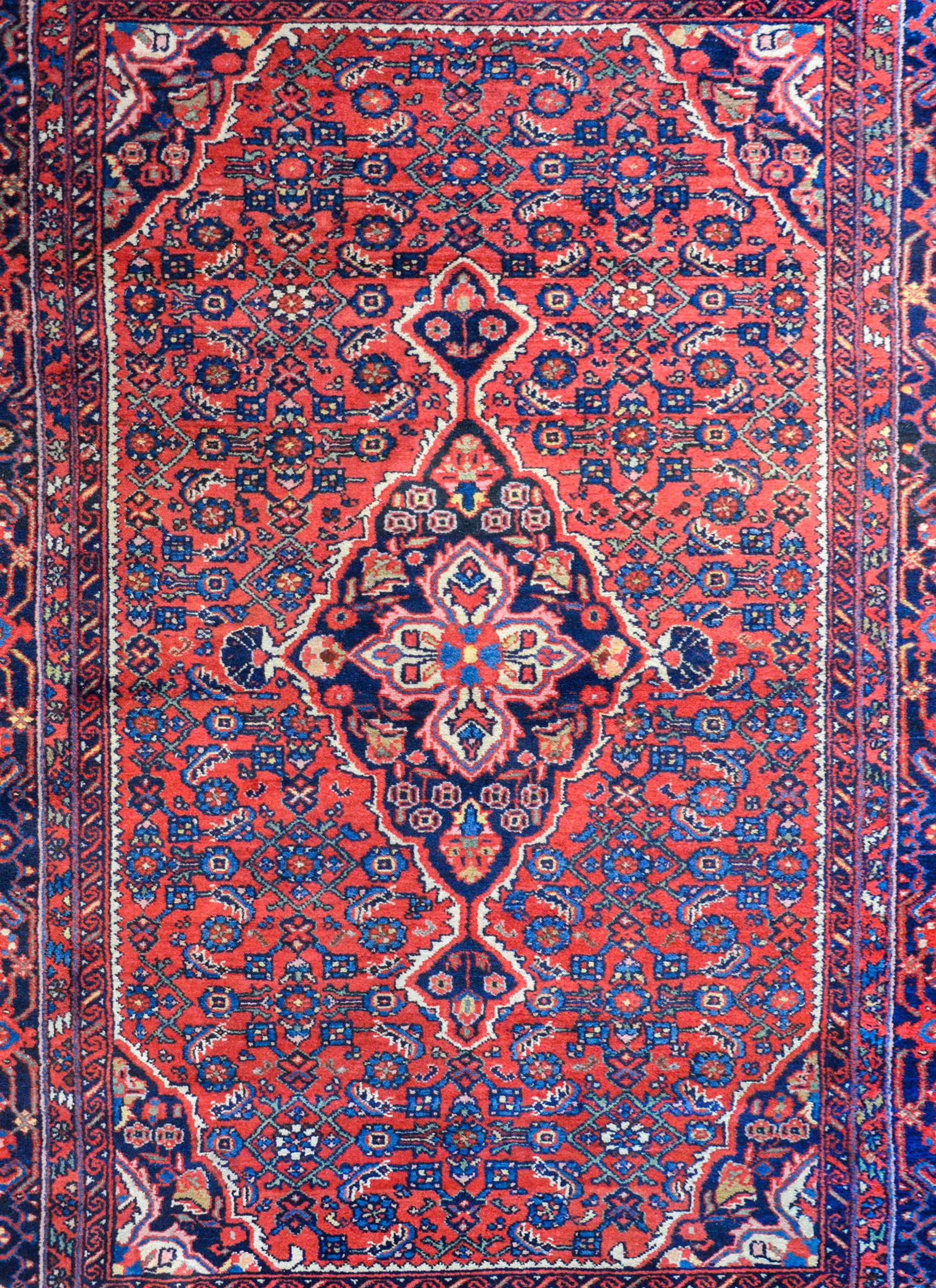 A wonderful early 20th century Persian Malayer rug with a large central diamond medallion on a field of trellis and myriad flowers all woven in light and dark indigo and white vegetable dyed wool on a crimson background. The border is wide with