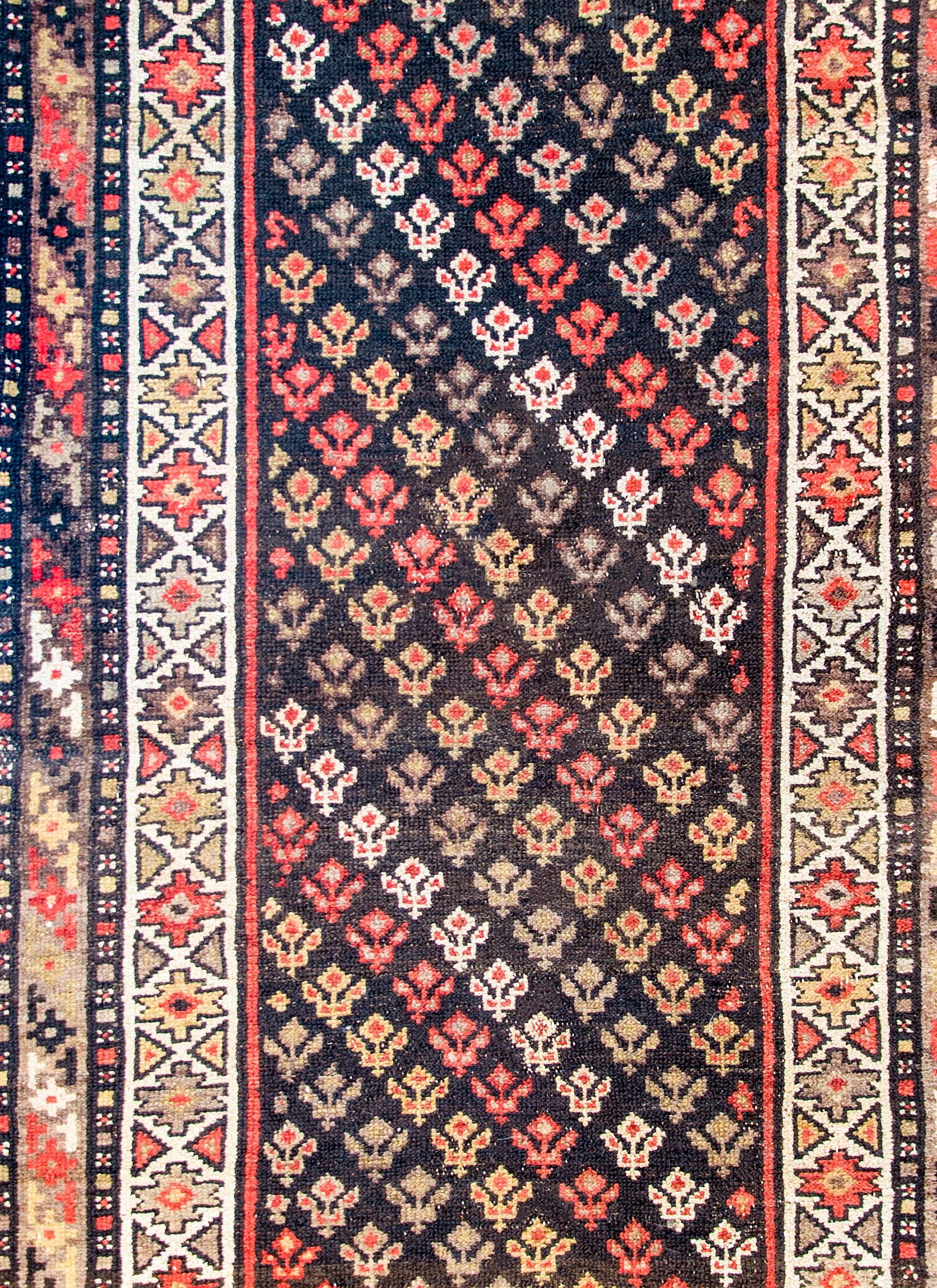 An early 20th century Persian Malayer runner with all-over tree-of-life pattern woven in alternating stripes of crimson, gold, white, and brown wool, on a black background, surrounded by multiple geometric and petite floral patterned borders.