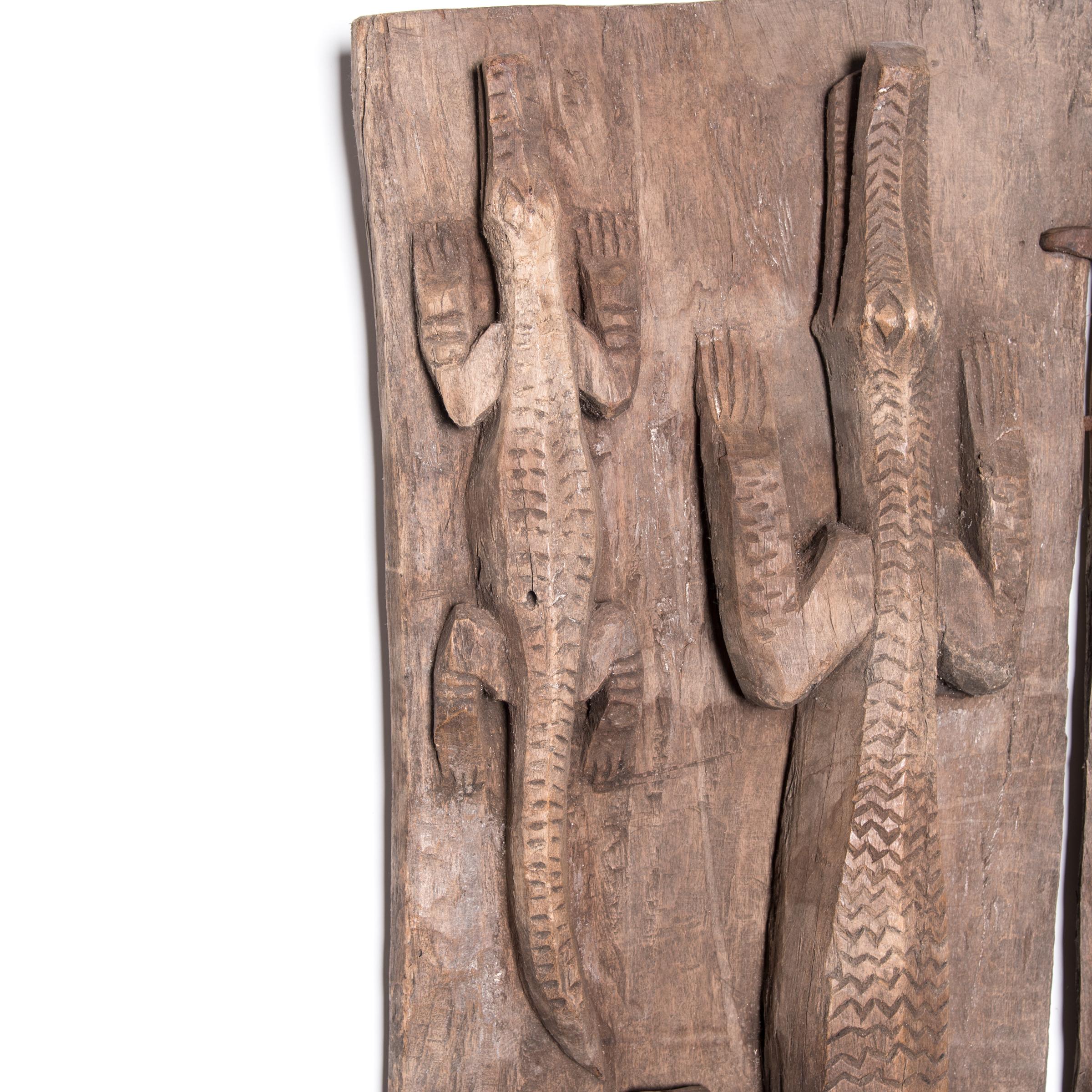 Carved directly out of the wood slating, these reptiles come to life, appearing to crawl up the door. Intricately textured with abstract patterns, the crawling reptiles bring a dynamic sense of movement to the otherwise rigid plank door. A crossbar