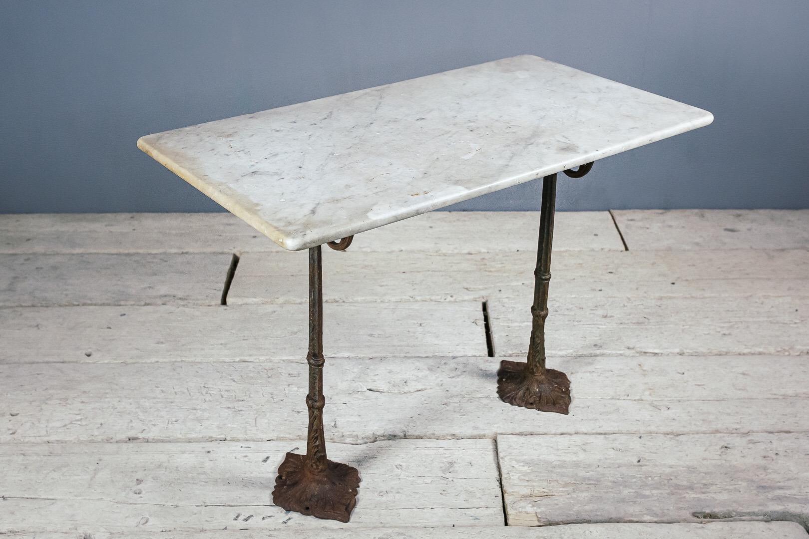 Cast iron and marble bistro table, remnant paint to the cast iron base and a good patina to the old marble top. This table comes as three pieces, two legs and the top which sits on top. The bases were historically fixed to the floor and ideally