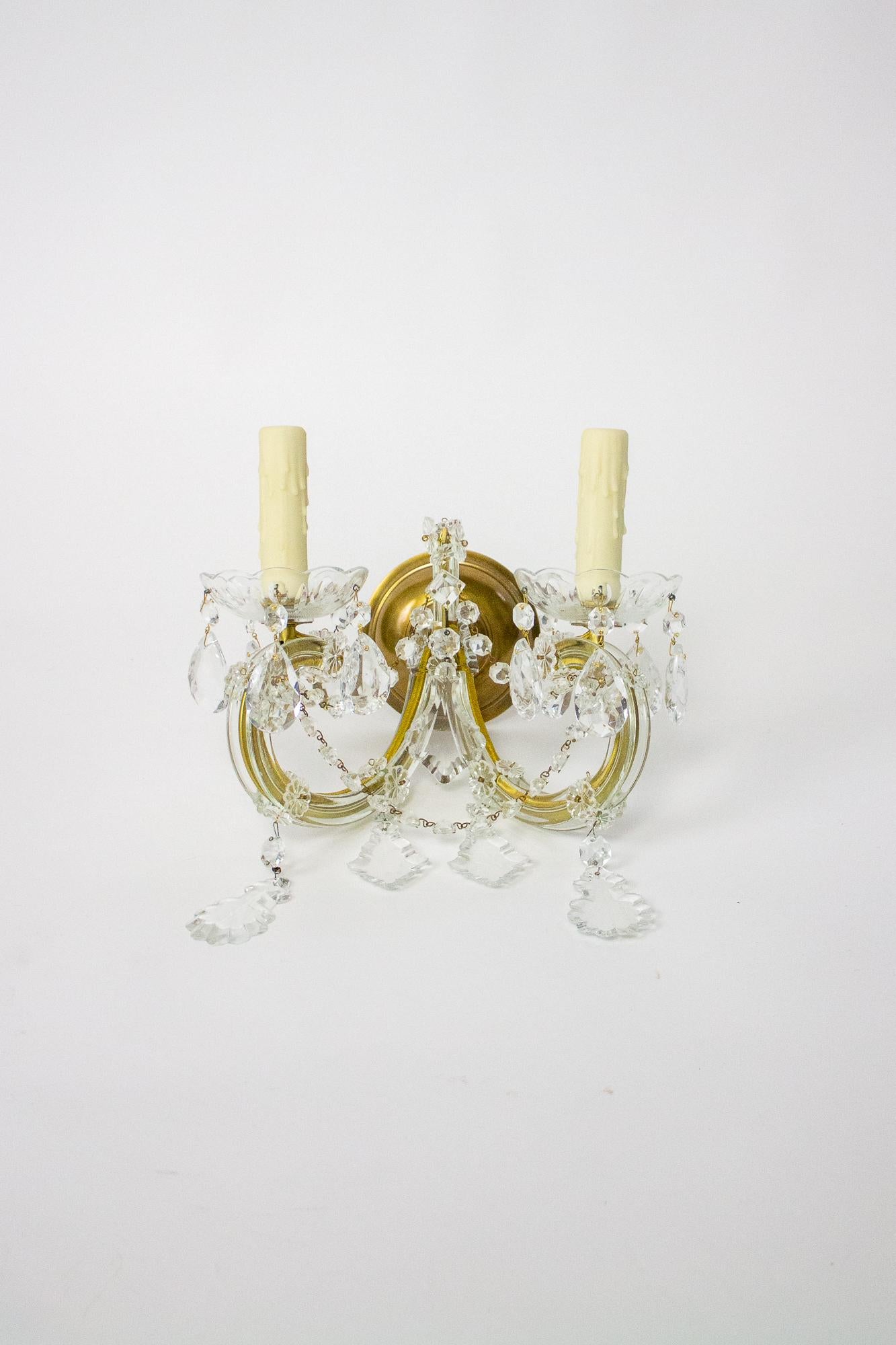 Pretty Maria Theresa Sconces with double curved arms. The arms are steel with a gold finish and are covered with glass tubing and rosettes. They meet in the center with a peak strung with rosettes and a crystal pendalogue. Cast glass bobeches have