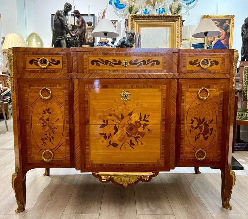 We present you this wonderful commode, designed during the transition period of Louis XV, boasting three drawers and three cabinets. Its marquetry depicts floral and foliage patters as well as musical instruments from the ancient times. It is a