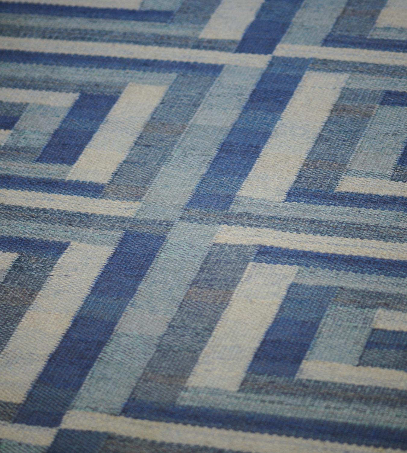 Ce tapis suédois vintage tissé à la main présente un champ bleu ton sur ton avec un motif général de bandes de couleurs nuancées reliées entre elles et formant une matrice à panneaux concentriques fantaisistes. Il s'agit d'un exemple exceptionnel de