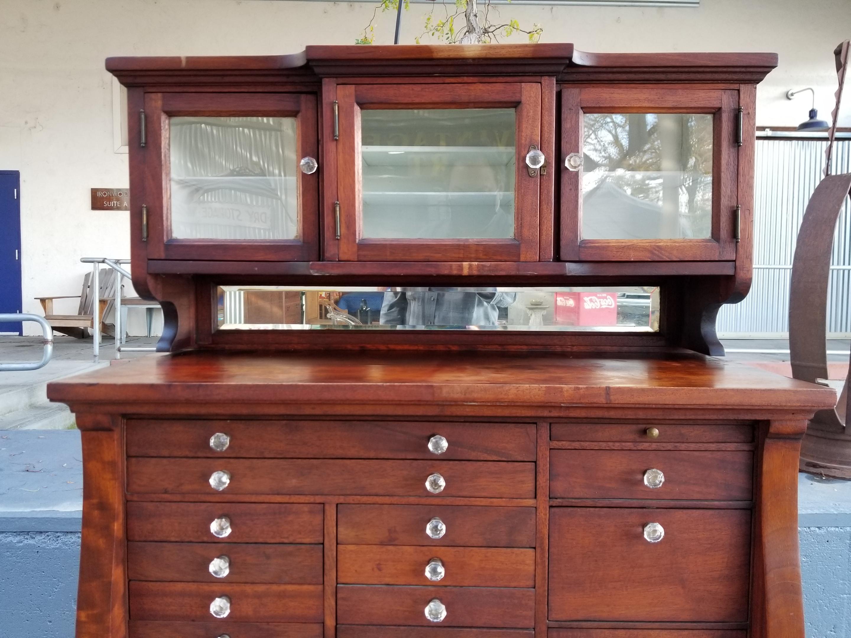 Impressive mahogany cabinet with ample storage for small items. Featuring 20 drawers, glass and wood panel doors and beveled glass back splash. All original pressed glass pulls are intact. These scarce cabinets were originally created for the