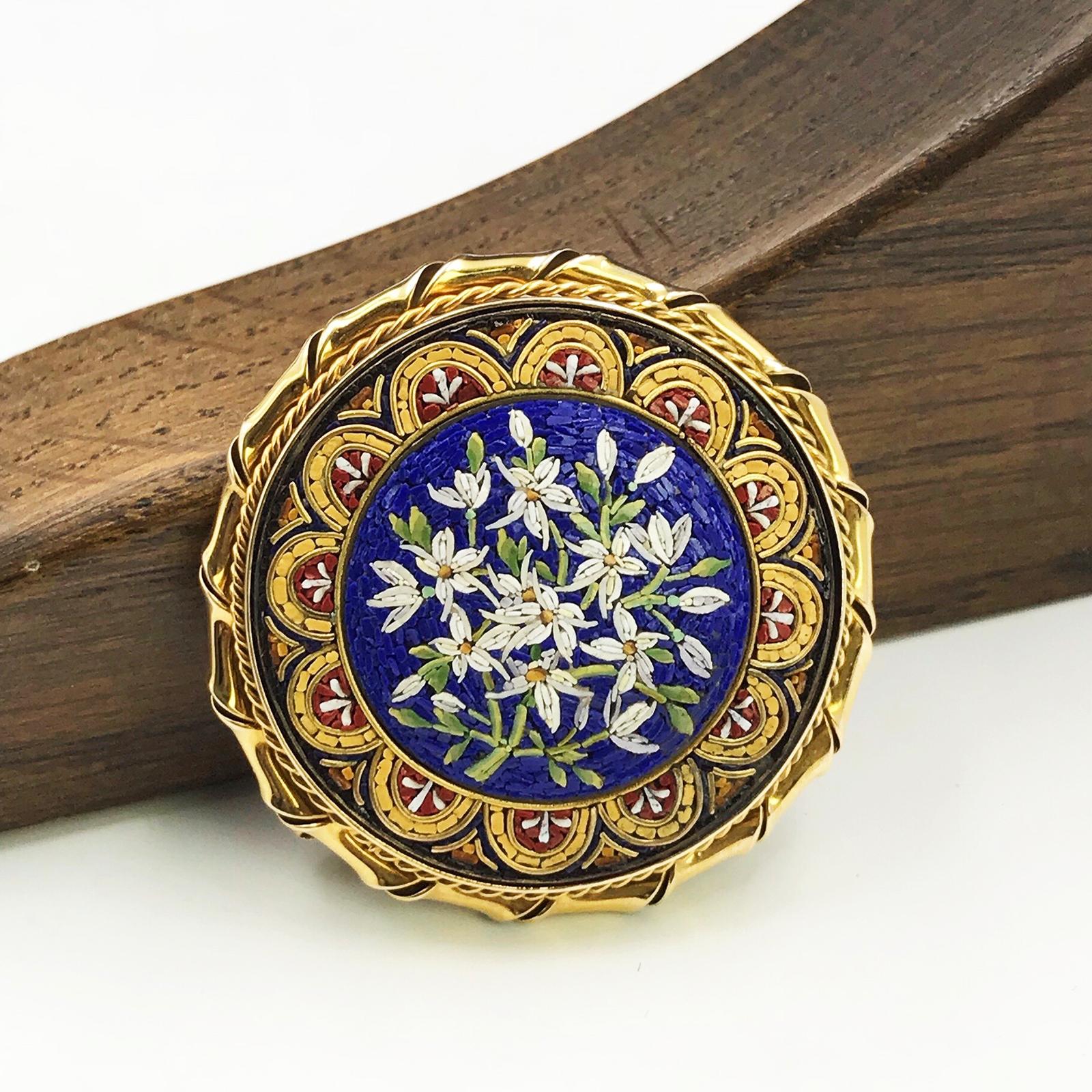 An early 20th century 9ct gold micro mosaic brooch. Of circular outline, the tesserae depicting flowers and buds, within a stylized foliate surround and scrolling border. May be worn as a pendant. Diameter 3.5cms. Weight 16gms. 