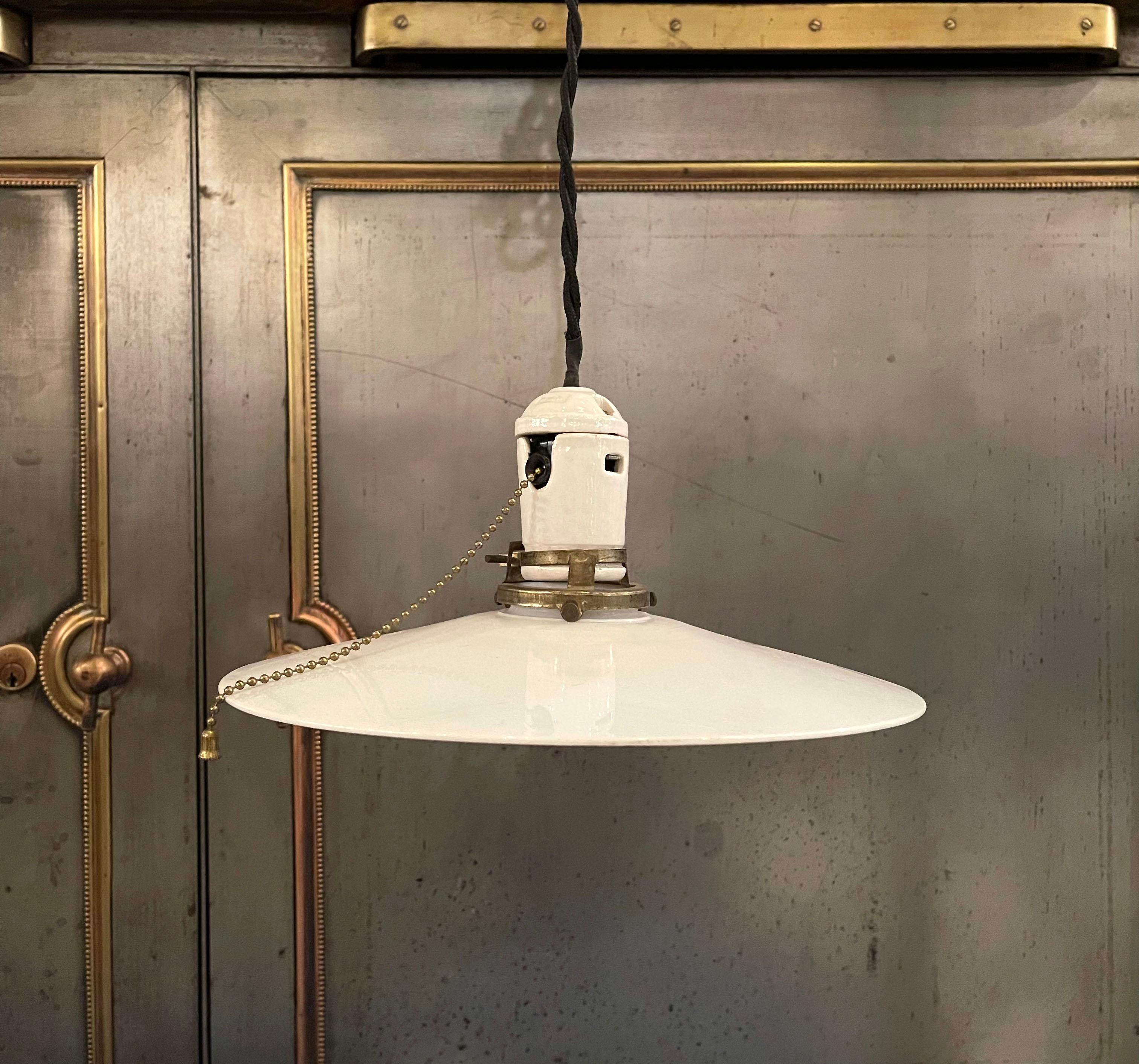 Early 20th century, industrial pendant light with 10.5 inch, hand-blown, milk glass disc shade, porcelain pull chain socket and brass fitter is newly wired with black braided cloth cord to hang at an overall lenght of 67.5 inches.