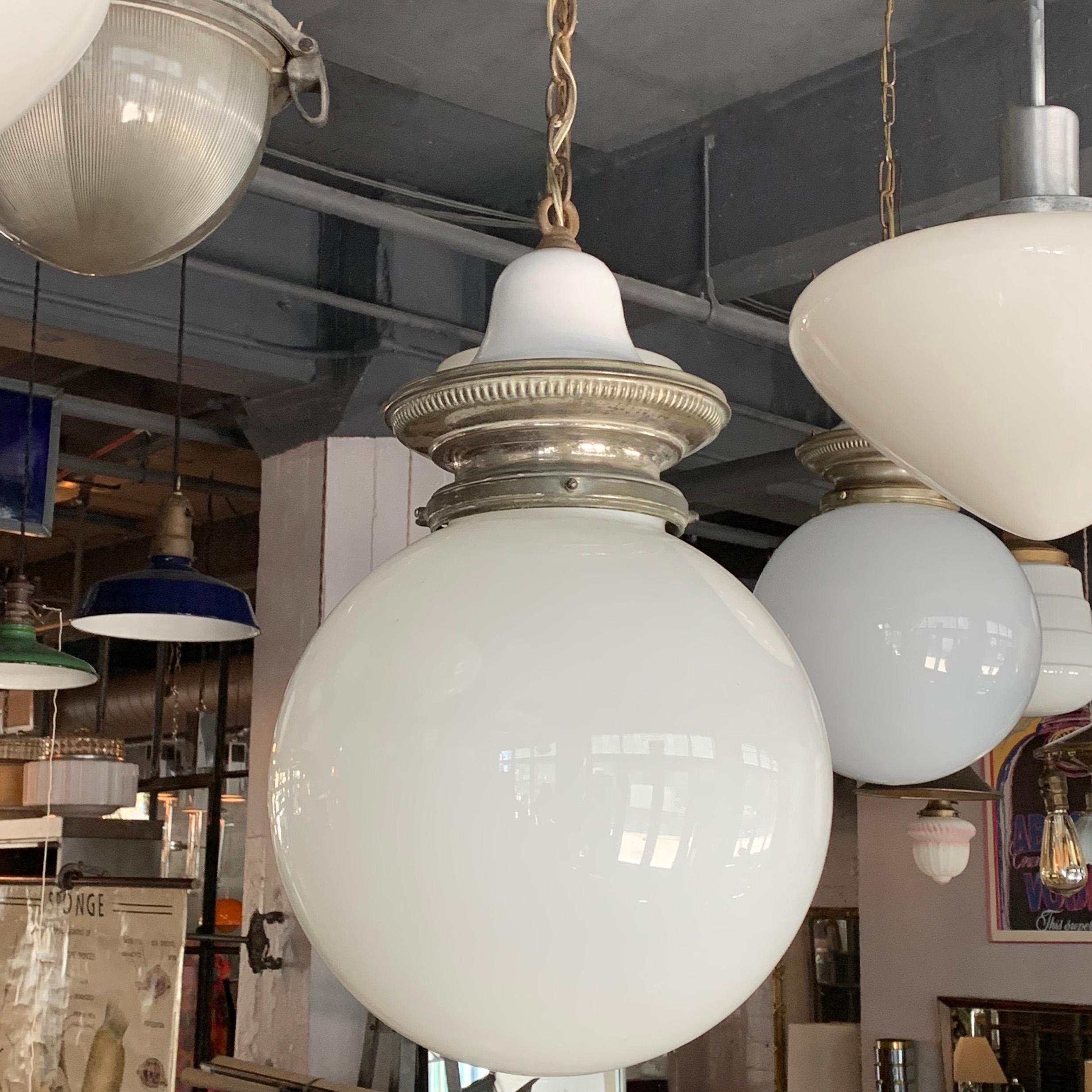 Early 20th century, industrial, library pendant light features a 13 inch milk glass globe shade with nickel-plated brass and porcelain enameled crown fitter, brass chain and canopy is wired to accept up to a 300 watt bulb. The overall height is 60