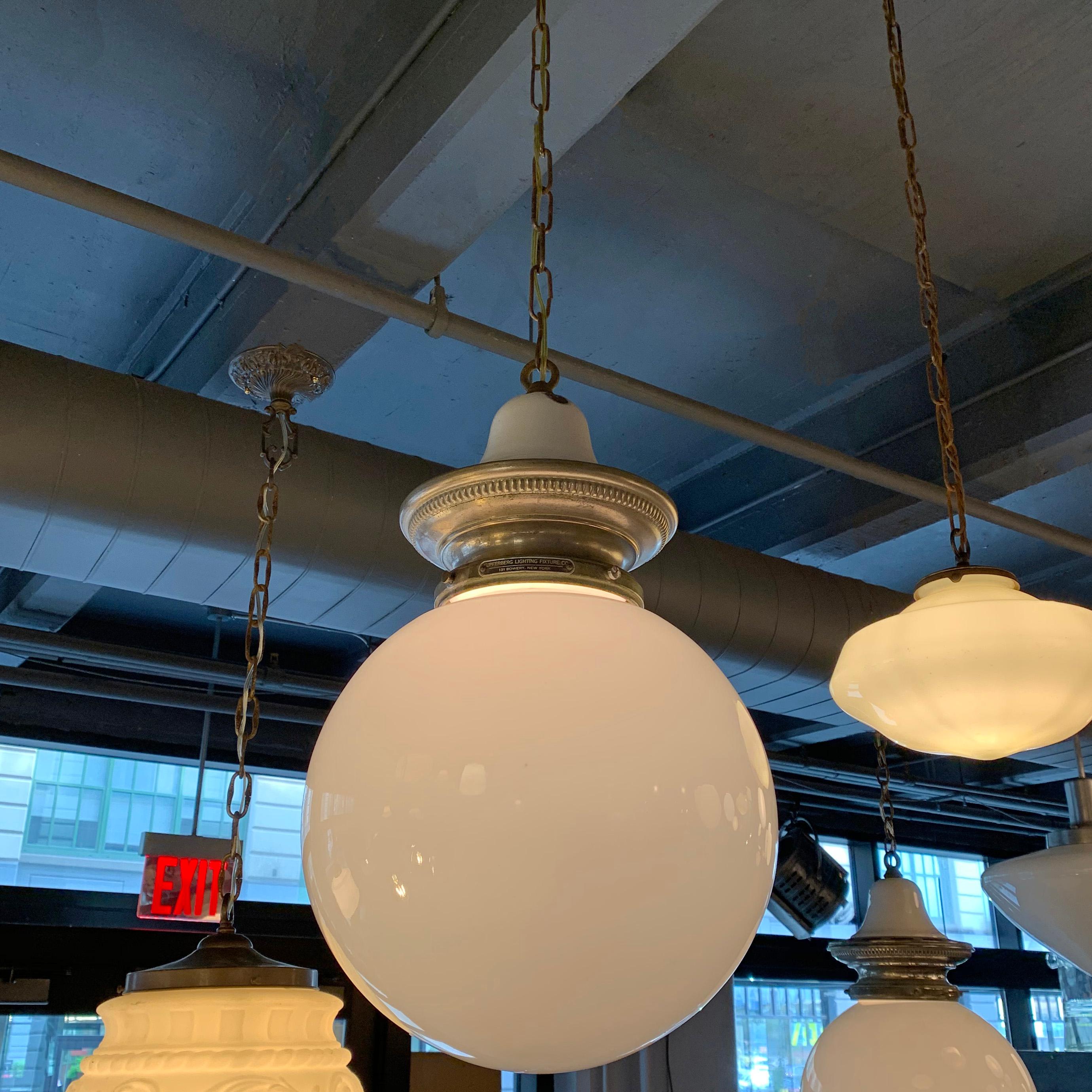 Early 20th century, industrial, library pendant light features a 12 inch milk glass globe shade with nickel-plated brass and porcelain enameled crown fitter, brass chain and canopy is wired to accept up to a 300 watt bulb. The overall height is 60