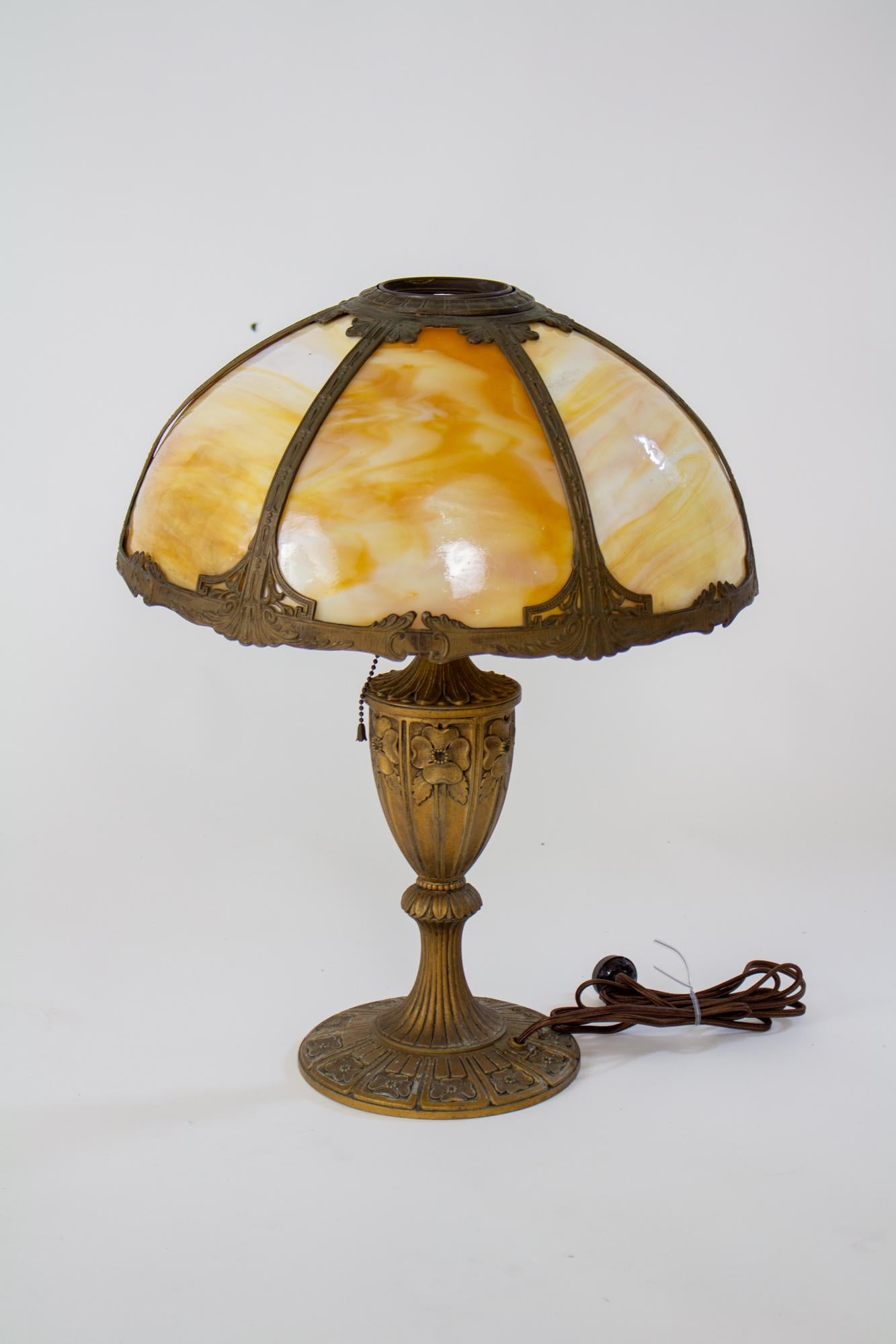 Early 20th Century Miller Arts and Crafts panel lamp with curved caramel glass. Curved six panel shade with swirled caramel slag glass. The base is urn shaped with flowers around the center and around the base. Signed, Edward Miller & Co. Cast metal