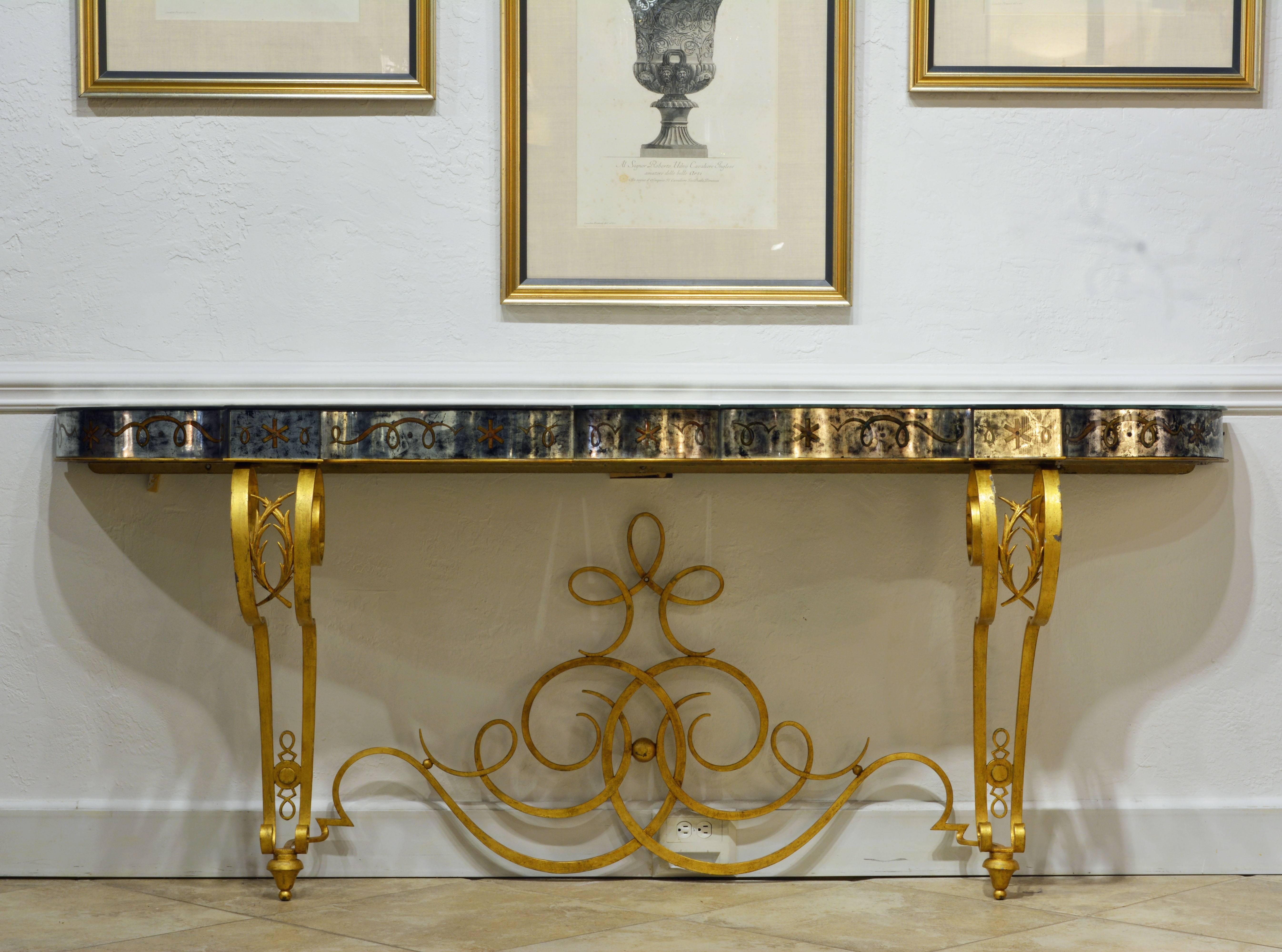 This superb and rare console table features an antiqued gilt inlaid mirrored top on a scrolled gilt iron frame in the manner of legendary French metal designer Raymond Subes (1893-1970). The top is shaped by serpentine and circular segments accented