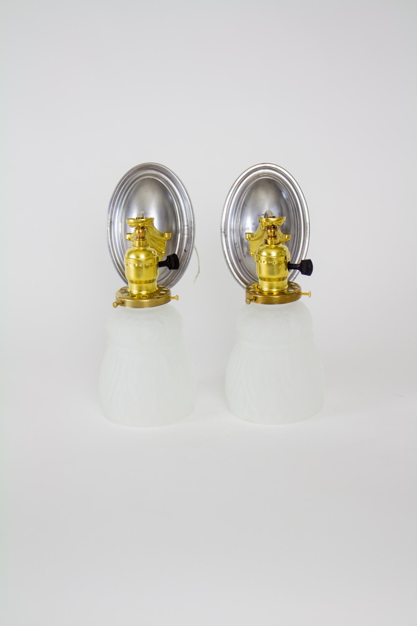 Early 20th Century mixed metal revival sconces with frosted glass - a pair. Oval backplate in steel with cast brass down hanging arm and a single light. Glass is a thick pressed frosted glass with a tulip form. Glass in excellent condition, some