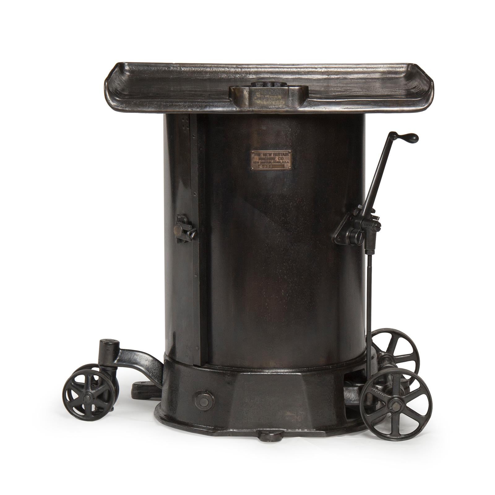 An Industrial vice stand or work table in patinated steel and cast iron with a drum shaped canister base on four (4) wheels.