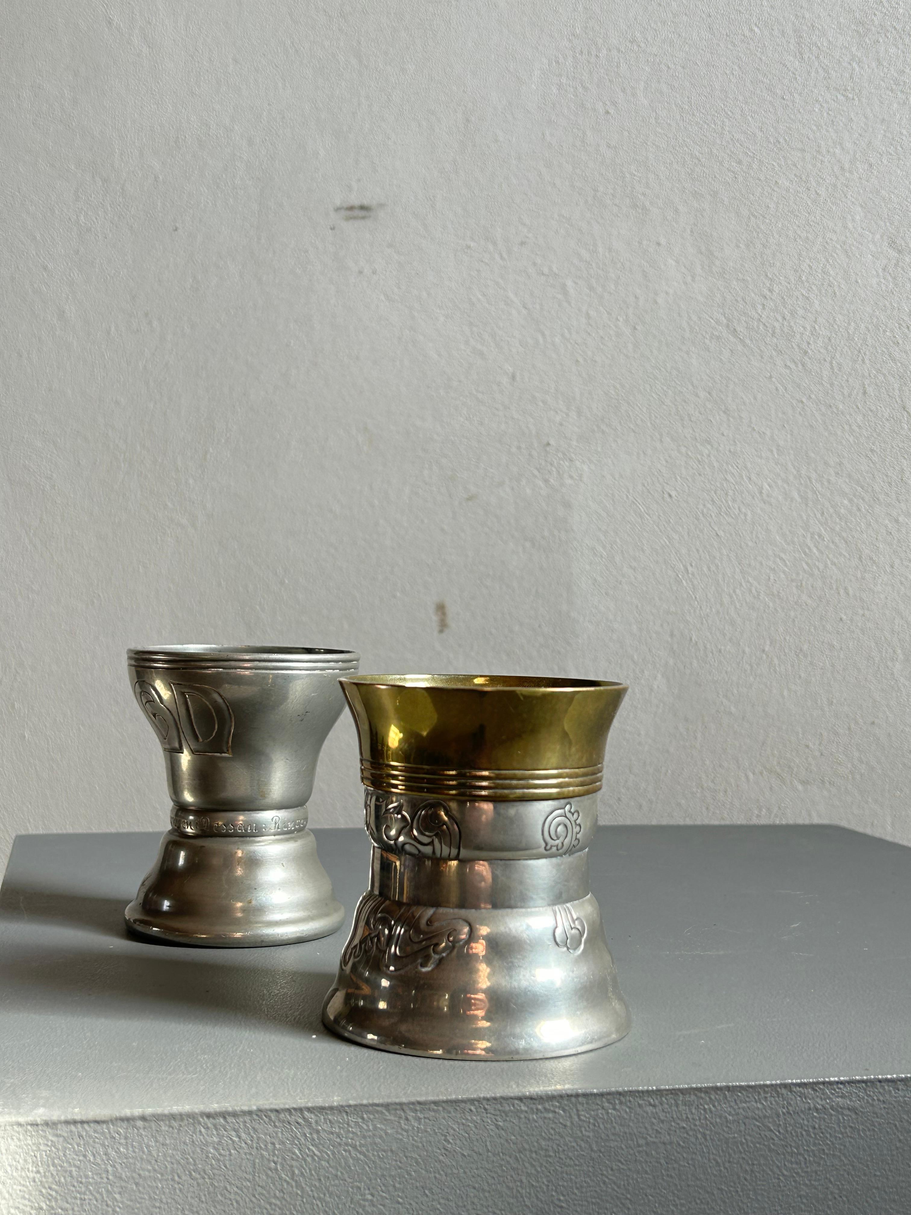 Un raro e documentato bicchiere in peltro e ottone dell'artista e metallurgico danese Mogens Ballin (1871-1914). Questo pezzo finemente lavorato esemplifica l'influenza del movimento Arts and Crafts in Danimarca, con la sua forma elegante, i