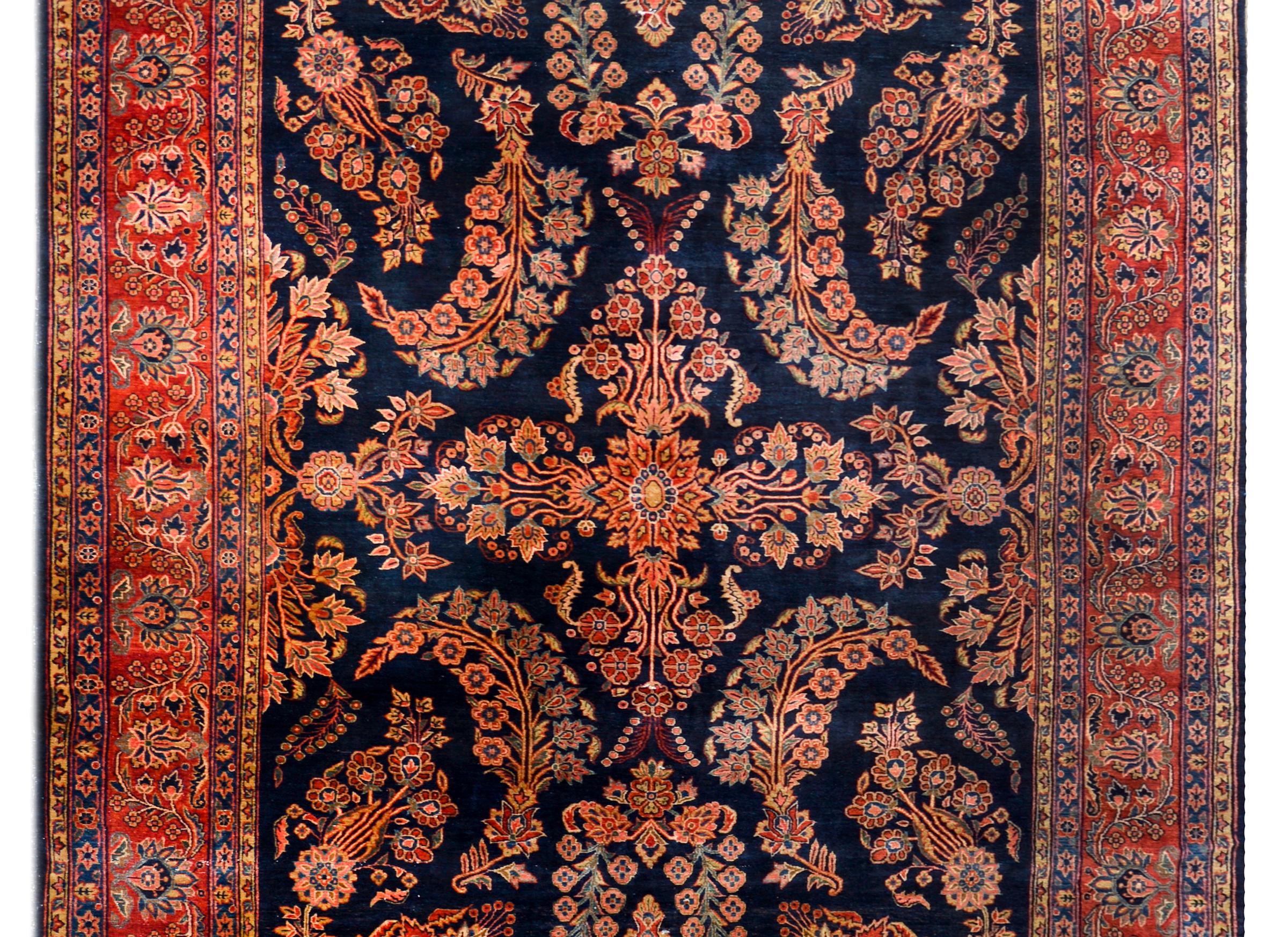 An incredible early 20th century Persian Mohajeran rug with a large-scale mirrored floral cluster pattern with pink, crimson, light and dark indigo, and cream, against a dark indigo background, and surrounded by a beautiful wide floral pattered