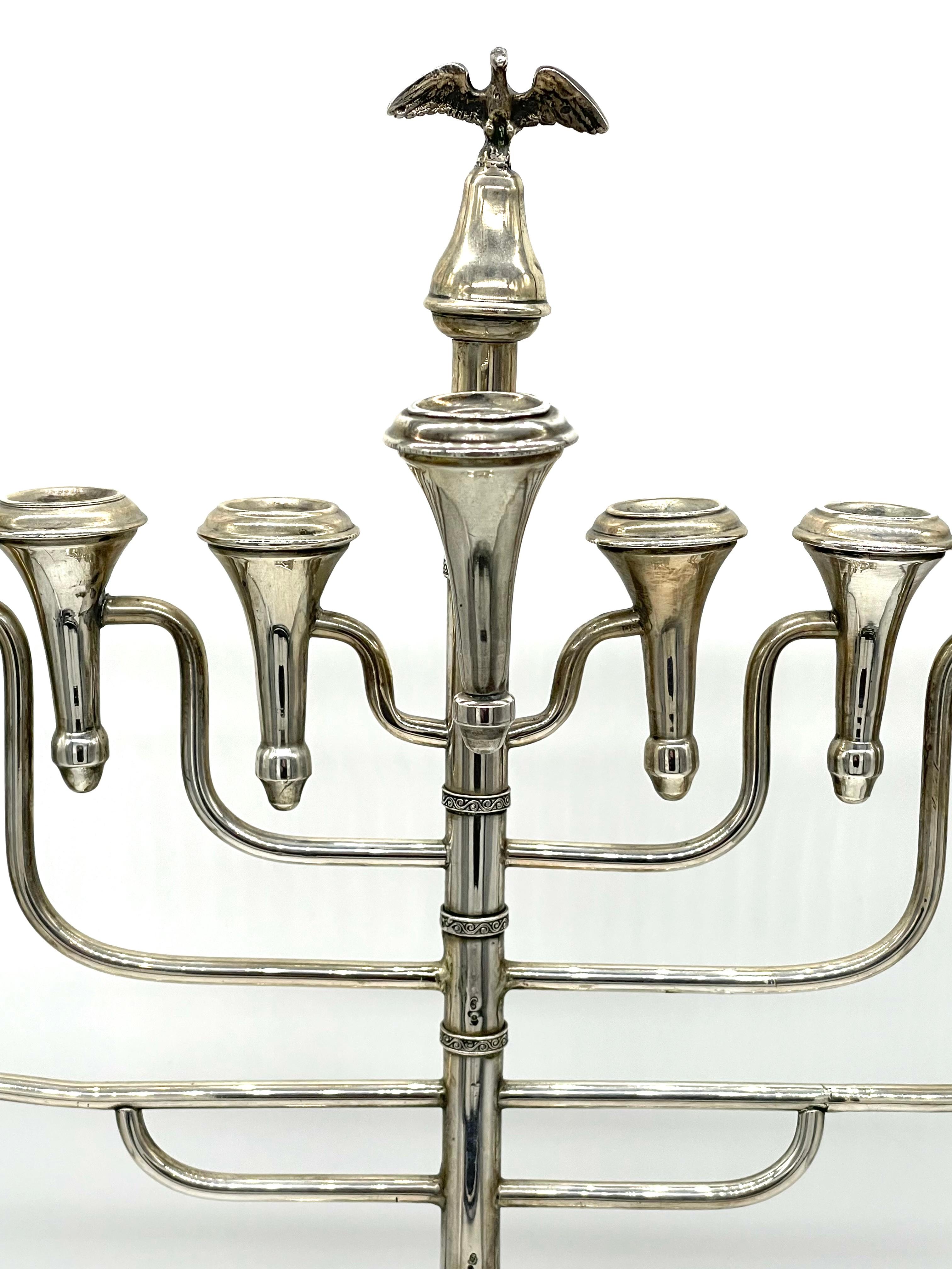Monumentale Chanukka-Lampe aus Silber aus dem frühen 20. Jahrhundert, hergestellt in Polen. Die im Art-Deco-Stil gestaltete Leuchte ist am Sockel mit floralen Motiven verziert, während sich an der Spitze der zentralen, tragenden Säule eine