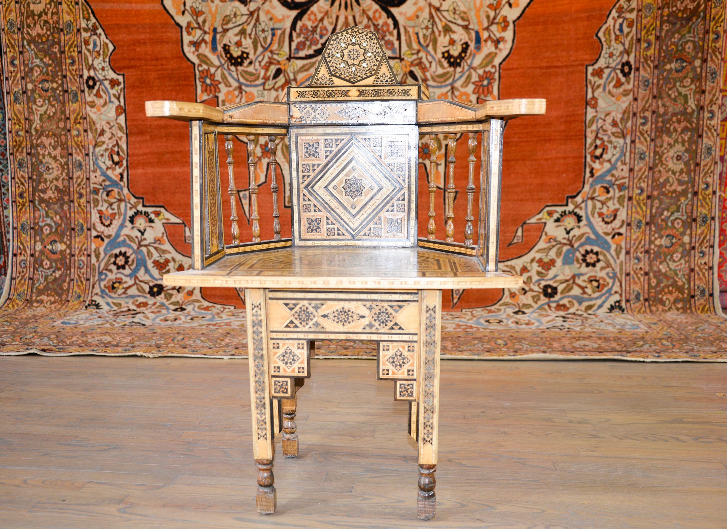An early 20th century Moroccan armchair with an elaborate pattern of repeated large and small eight-point stars executed in inlaid exotic and ebonized woods and mother-of-pearl. The sloping arms are supported by turned spindles, and the legs are