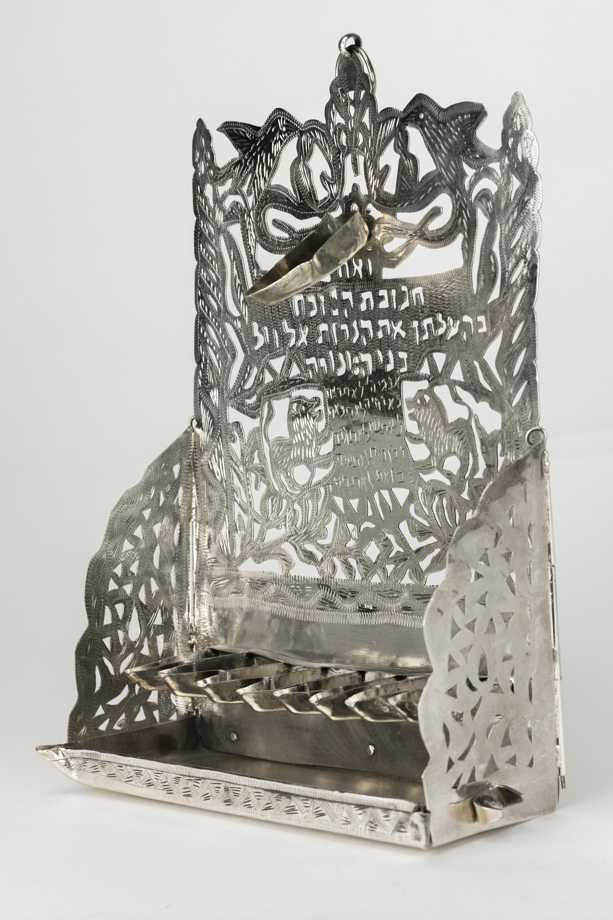Handmade silver Hanukkah lamp, Morocco, circa 1910. 
Cutout and engraved back plate with dense vegetal patterns at the bottom, two lions flaking the Table of Decalogue at the center, two pillars on the sides, and two birds above the Shamsh. Two sawn