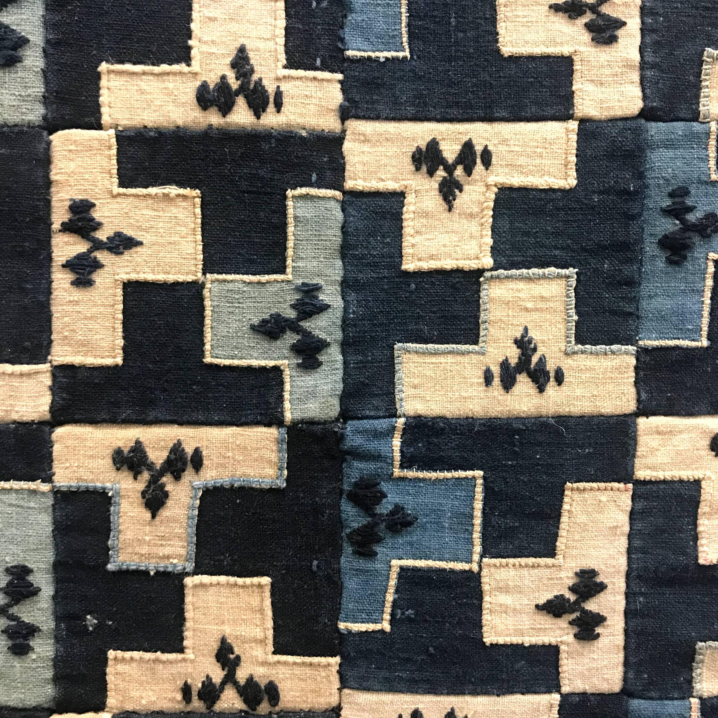 A wonderful early 20th century Chinese Minority indigo panel comprised of multiple embroidered squares pieced together to create an all-over meandering motif pattern, framed with a solid indigo band, and stretched over a simple stretcher. This panel