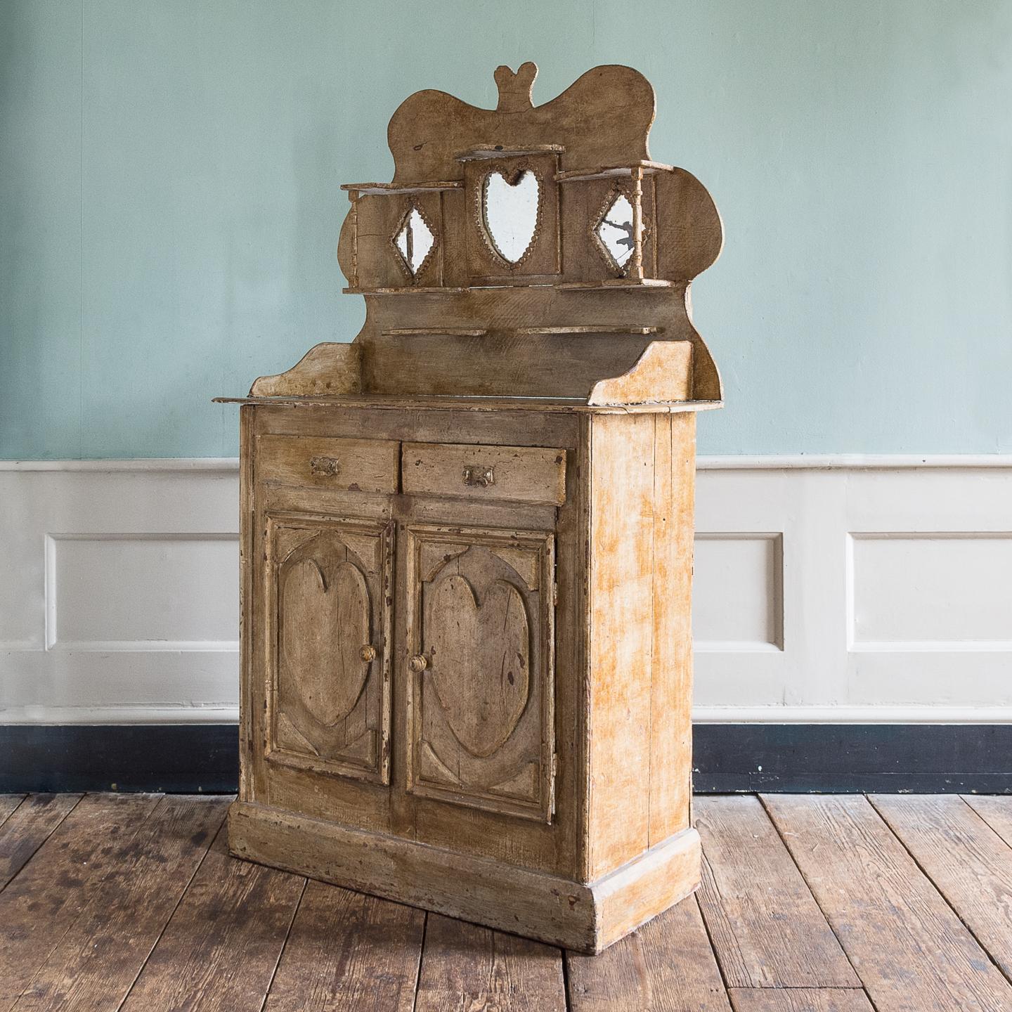 Early 20th century tramp art dresser, with all over scumble glaze, the back-board with an arrangement of shelves and mirrors, constructed from re-used packing cases. 

The origin of this piece is not certain but the printing of the crates used to